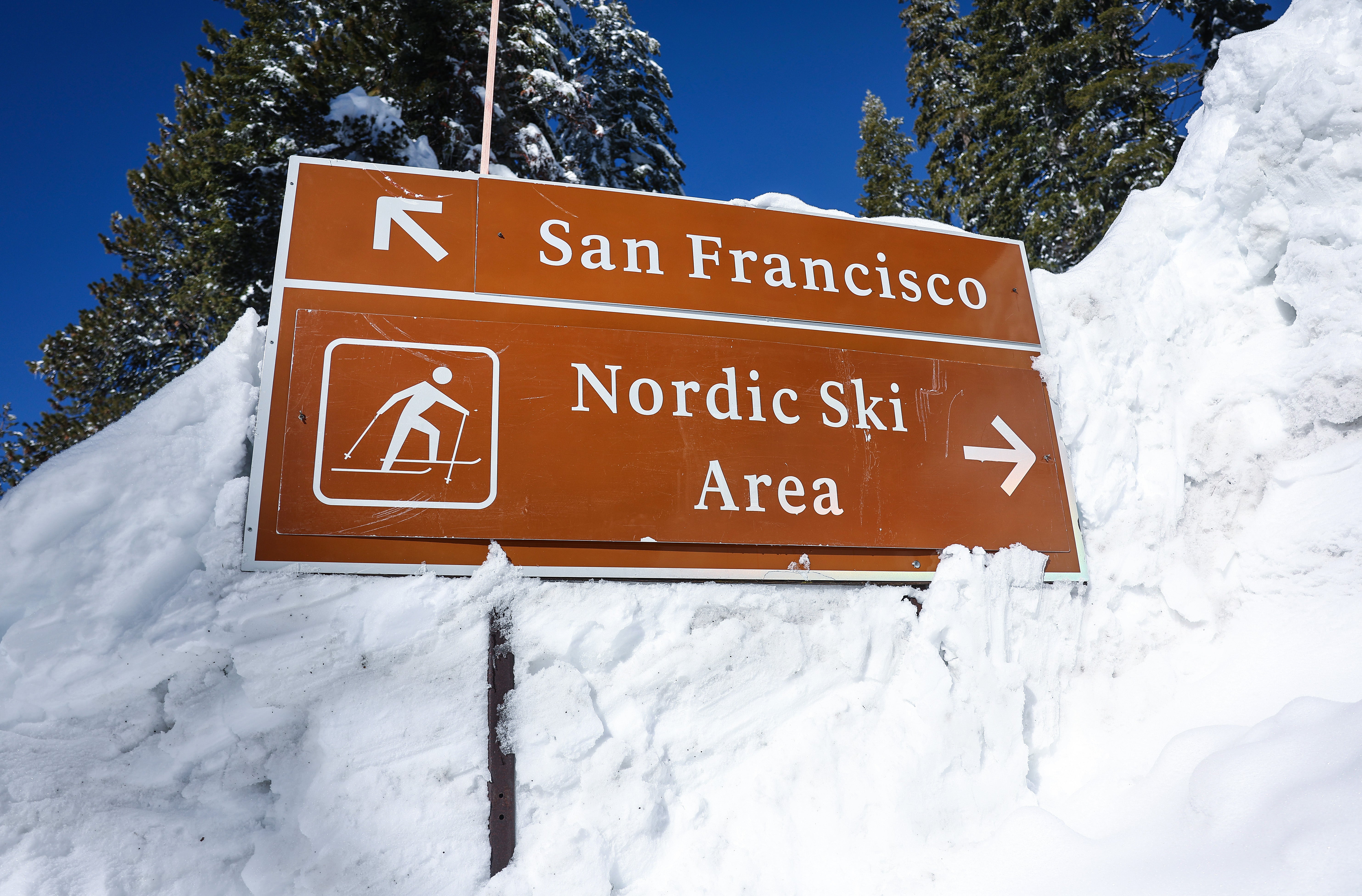 A road sign pointing towards San Francisco and a ski area is partially buried in a snowbank after a series of atmospheric river storms on January 20, 2023 in Yosemite National Park, California