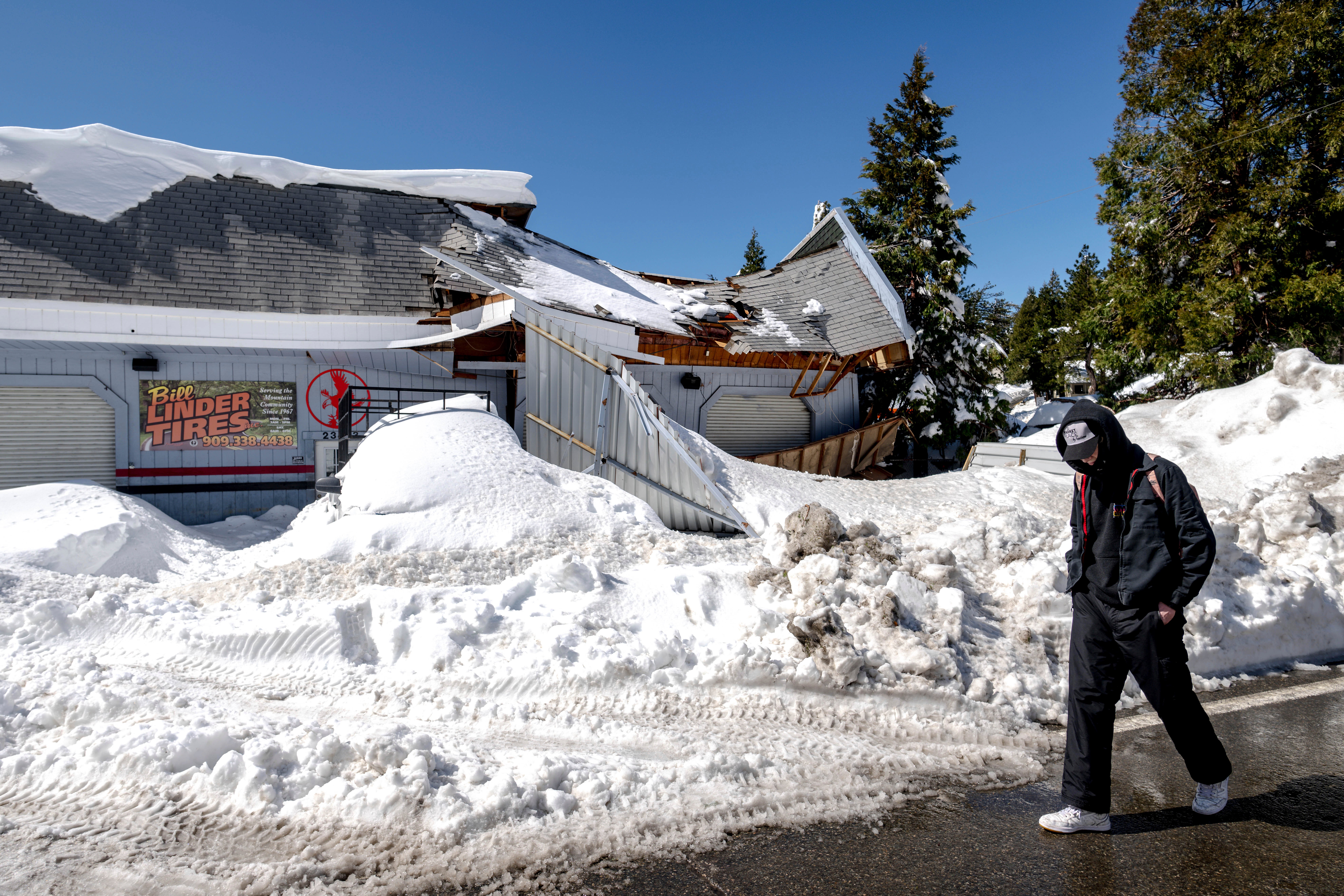 A man walks past a damaged tire shop in Crestline, Calif., Friday, March 3, 2023, following a huge snowfall that buried homes and businesses. (Watchara Phomicinda/The Orange County Register via AP)