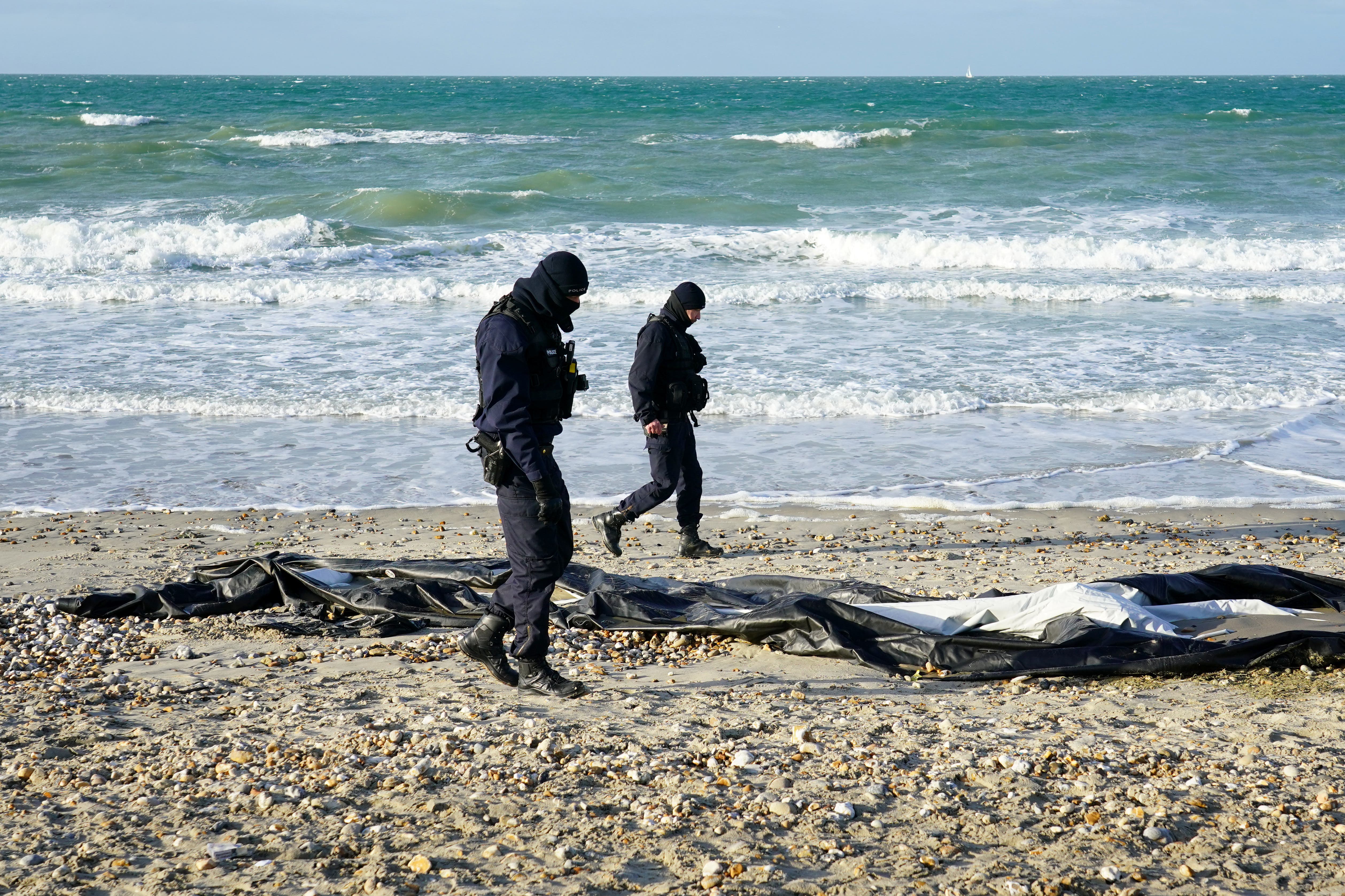 French police officers pass a deflated dinghy on the beach in Wimereux near Calais (Gareth Fuller/PA)