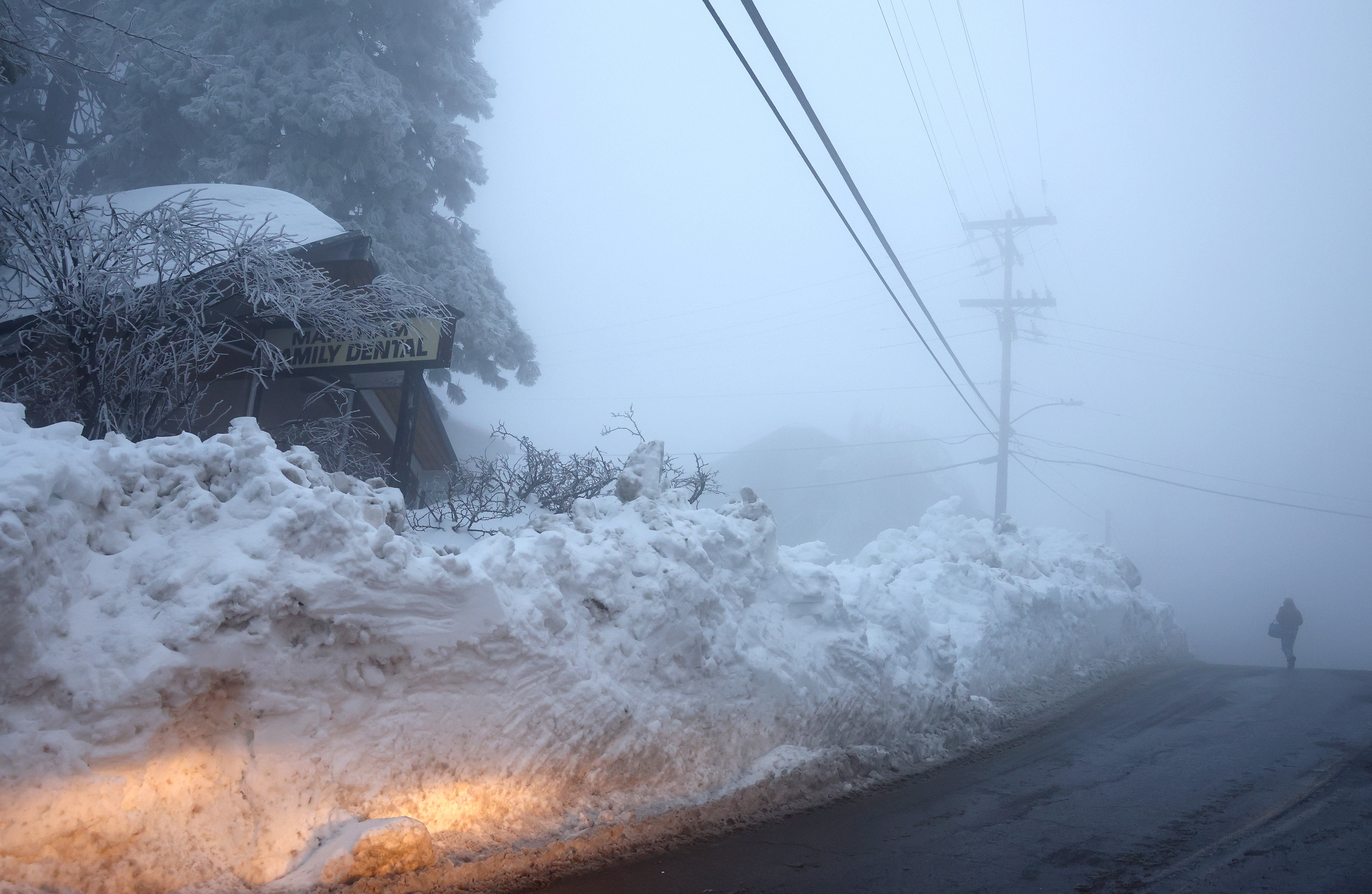 A person walks near a snow berm on 6 March in front of a dental office after a series of winter storms dropped more than 100 inches of snow in the San Bernardino Mountains in Southern California