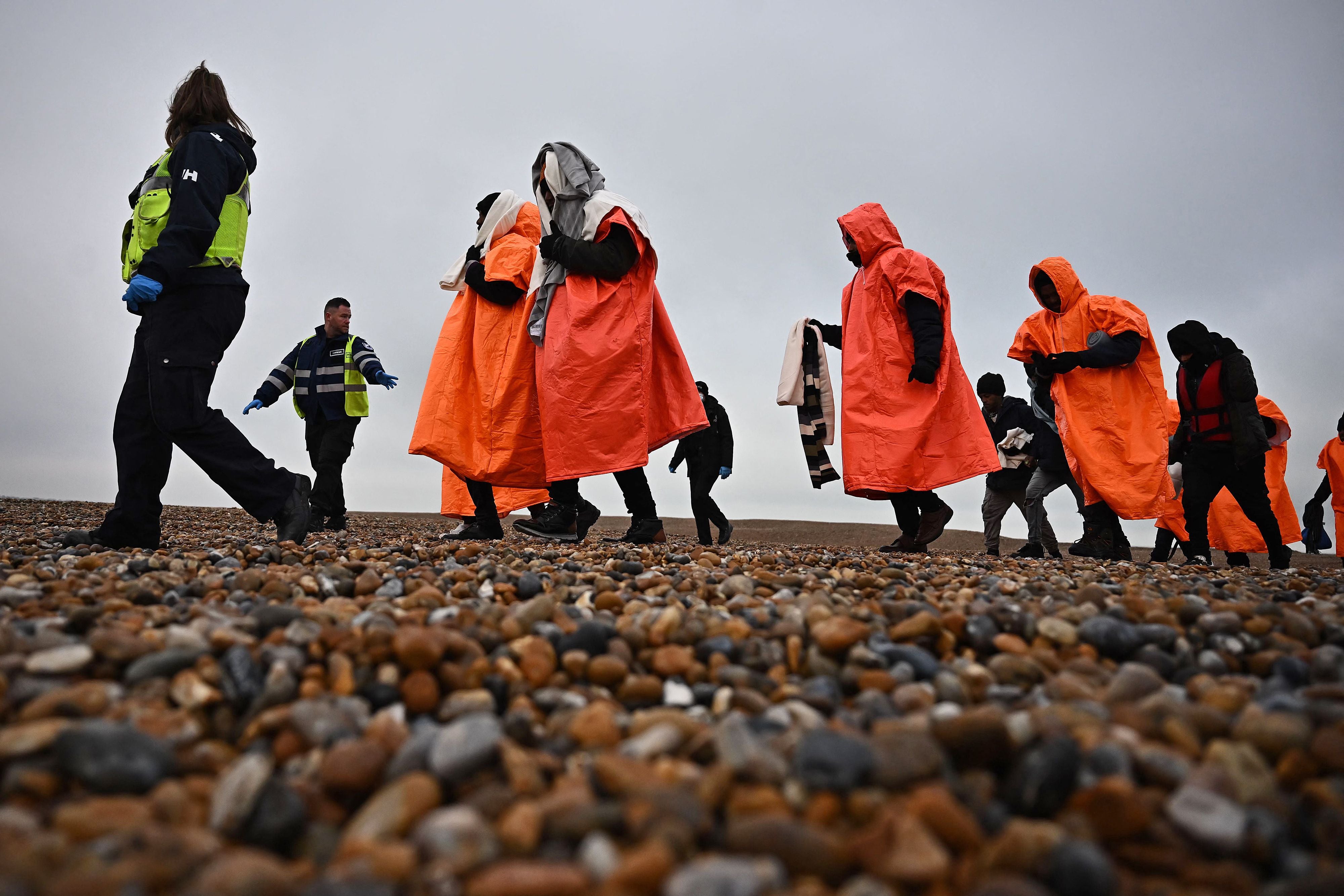 Immigration officers escort migrants on the shore at Dungeness