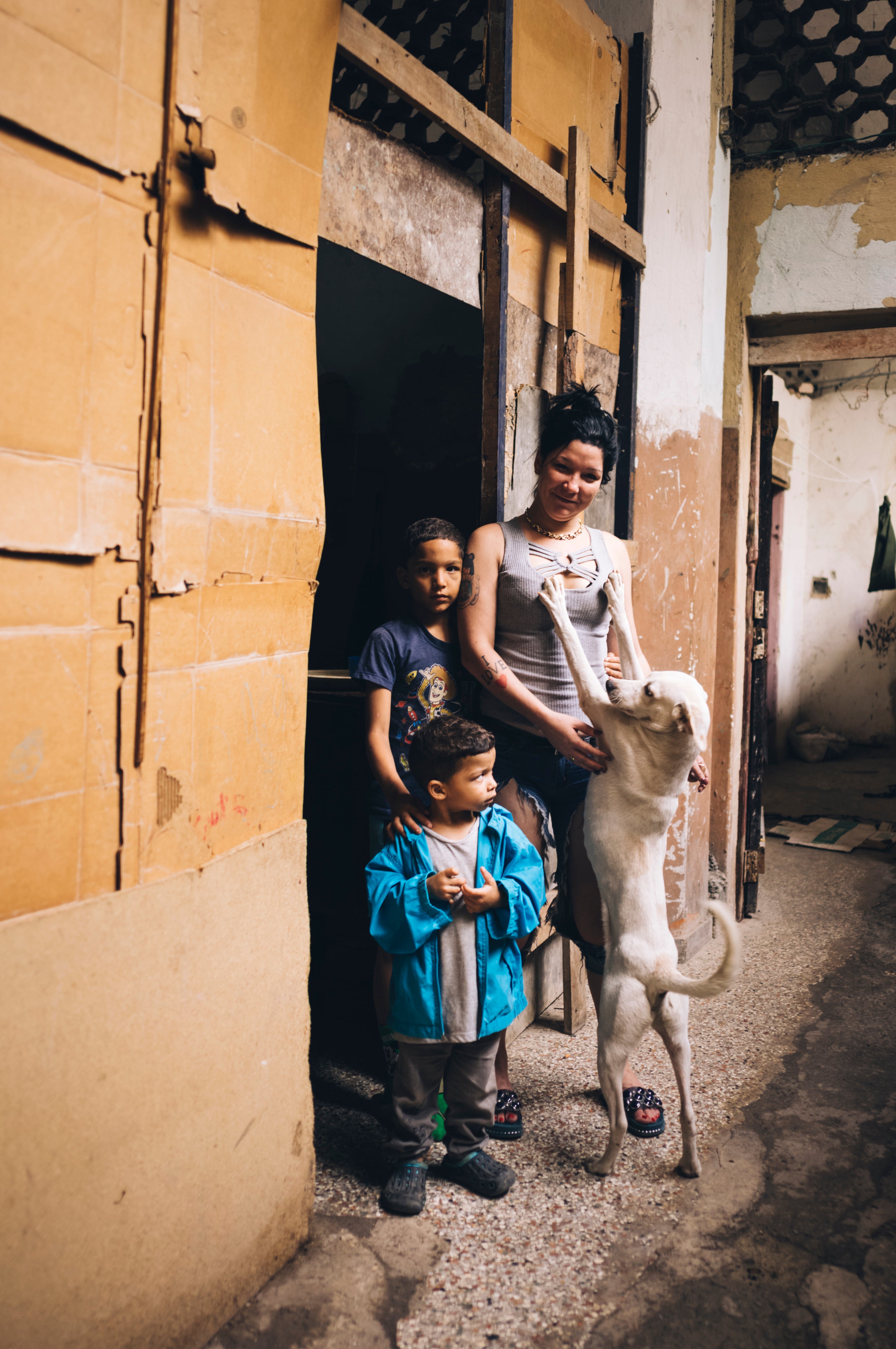 A mother of two and their dog Blanco pose for a portrait in the doorway of their living quarters in a Centro Habana albergue