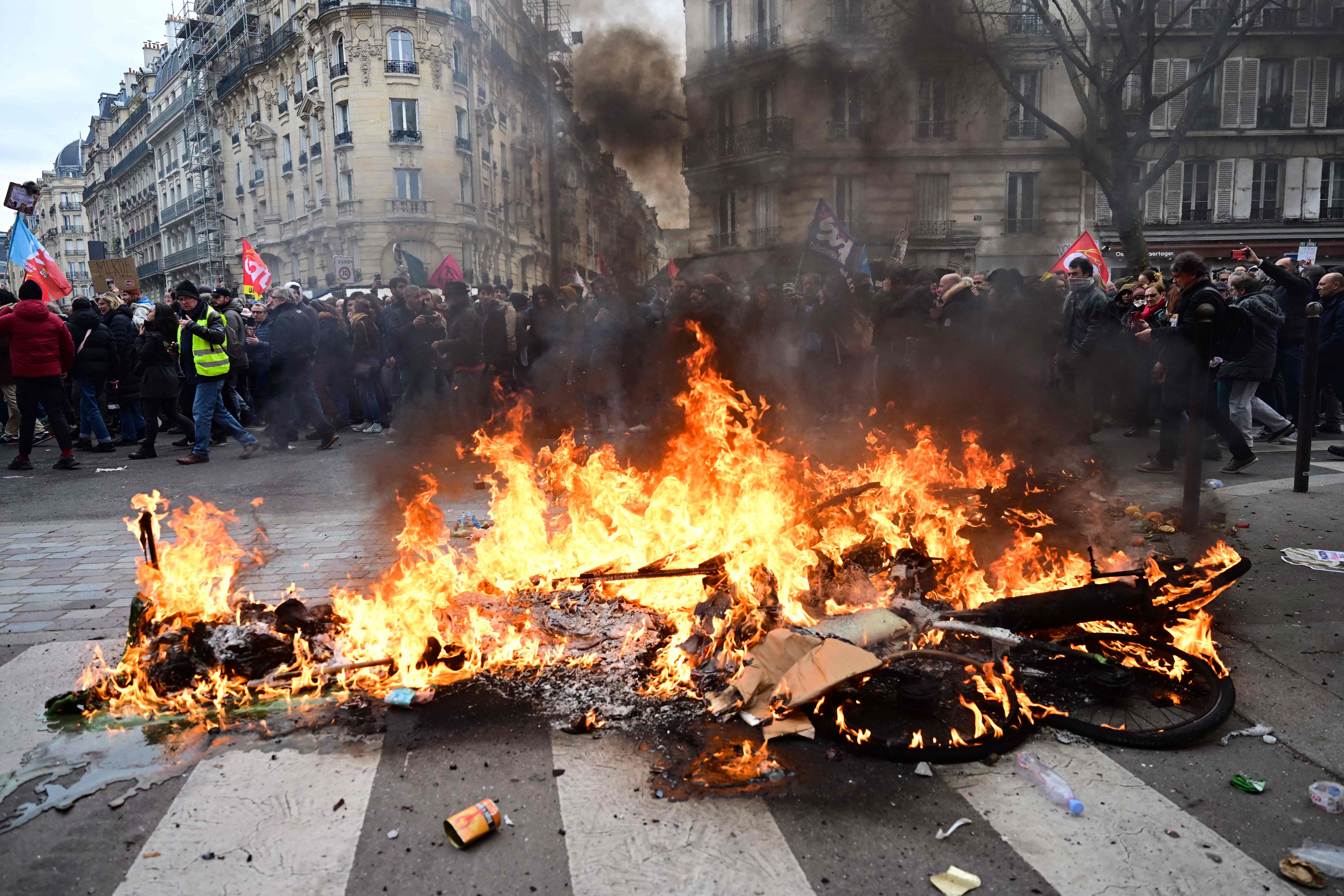 Protetsors walk past a fire during a demonstration, as part of a nationwide day of strikes and protests called by unions over the proposed pensions overhaul, in Paris