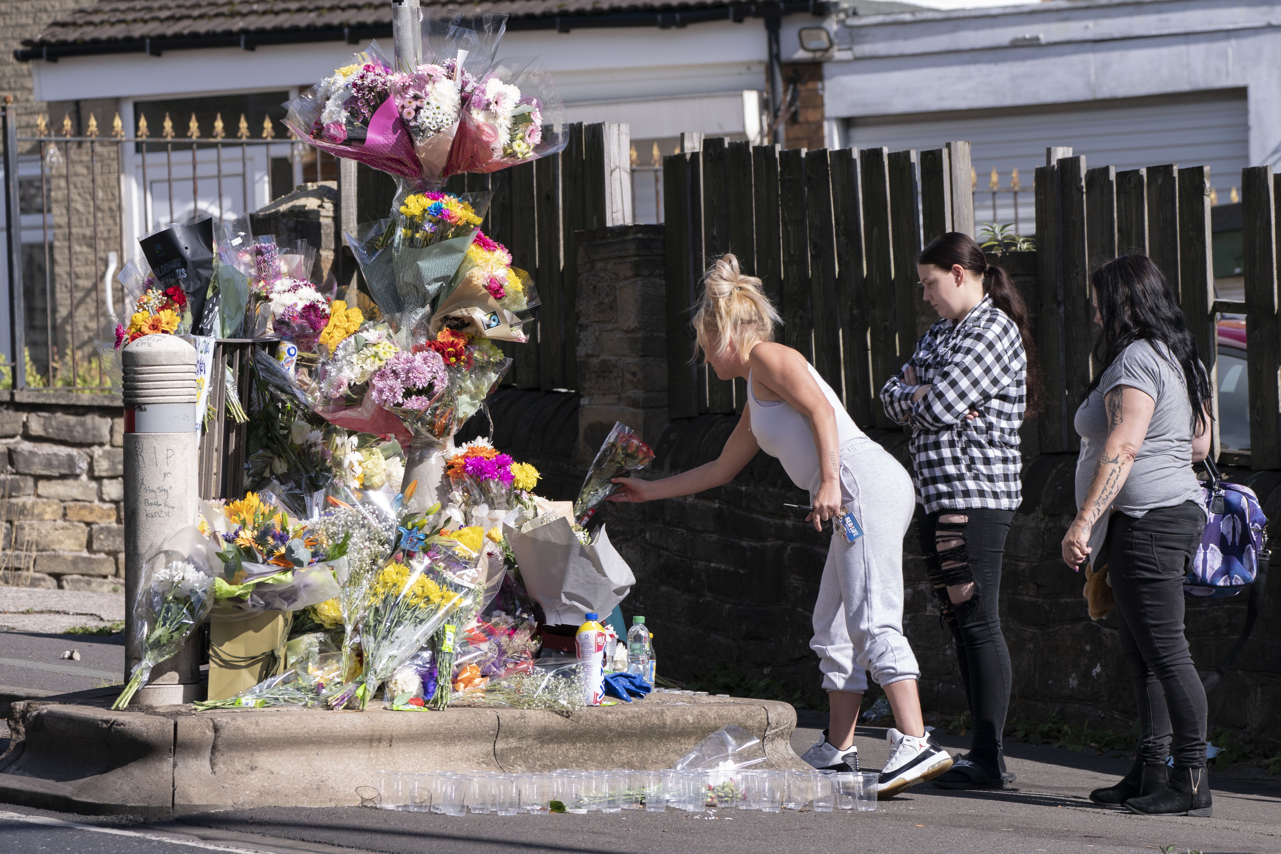 People lay a floral tributes at the scene in Woodhouse Hill, Huddersfield, where 15-year-old schoolboy Khayri McLean was fatally stabbed outside his school gates (PA)