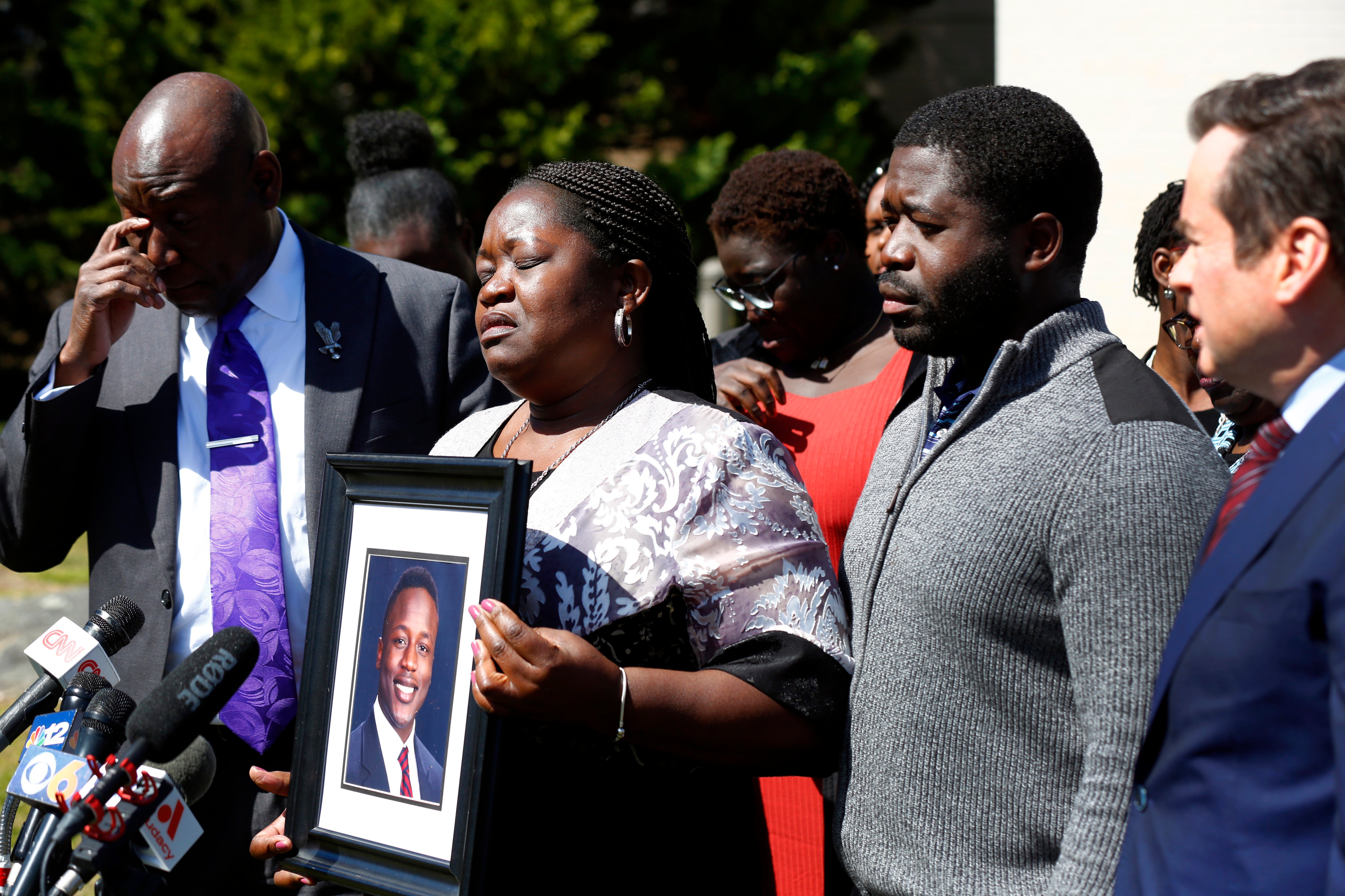 Caroline Ouko, mother of Irvo Otieno, holds a portrait of her son with attorney Ben Crump, left, her older son, Leon Ochieng and attorney Mark Krudys at the Dinwiddie Courthouse in Dinwiddie, Virginia