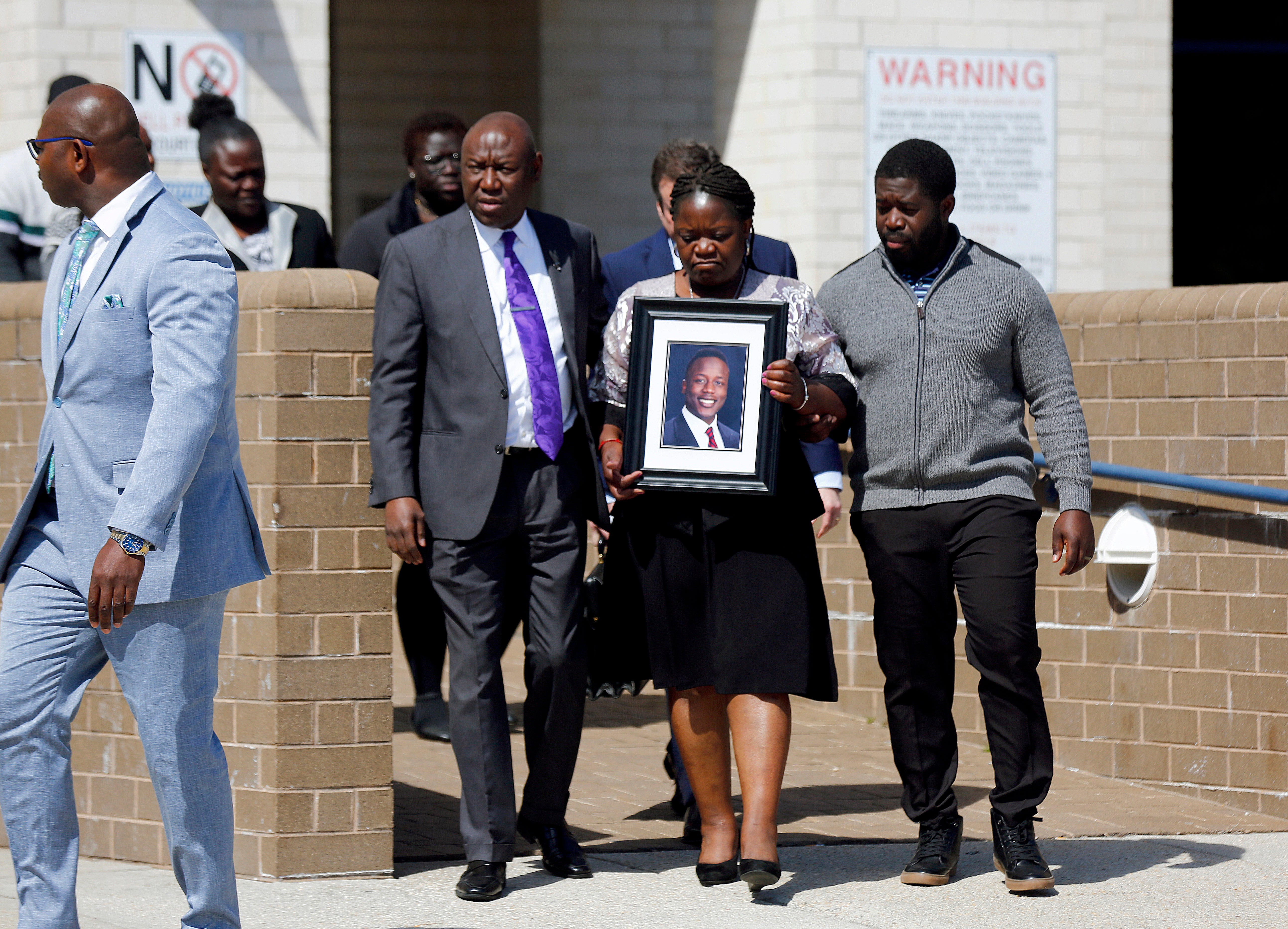 Caroline Ouko, mother of Irvo Otieno, holds a portrait of her son as she walks out of the Dinwiddie Courthouse with attorney Ben Crump