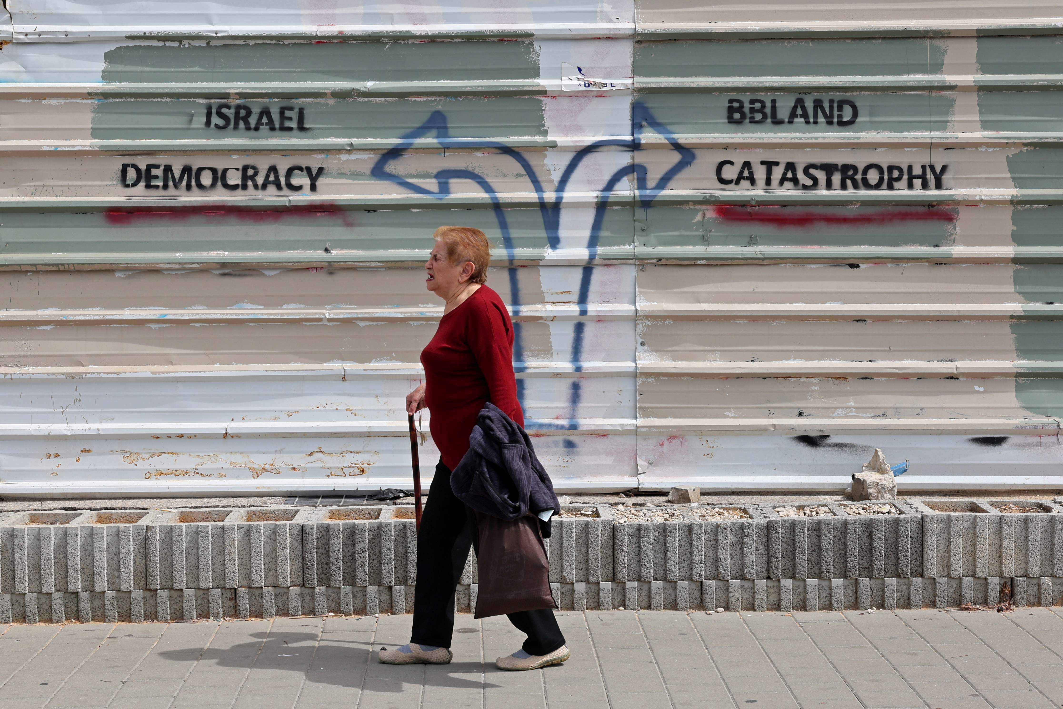 A woman walks past a graffiti during ongoing demonstrations in Tel Aviv on Thursday