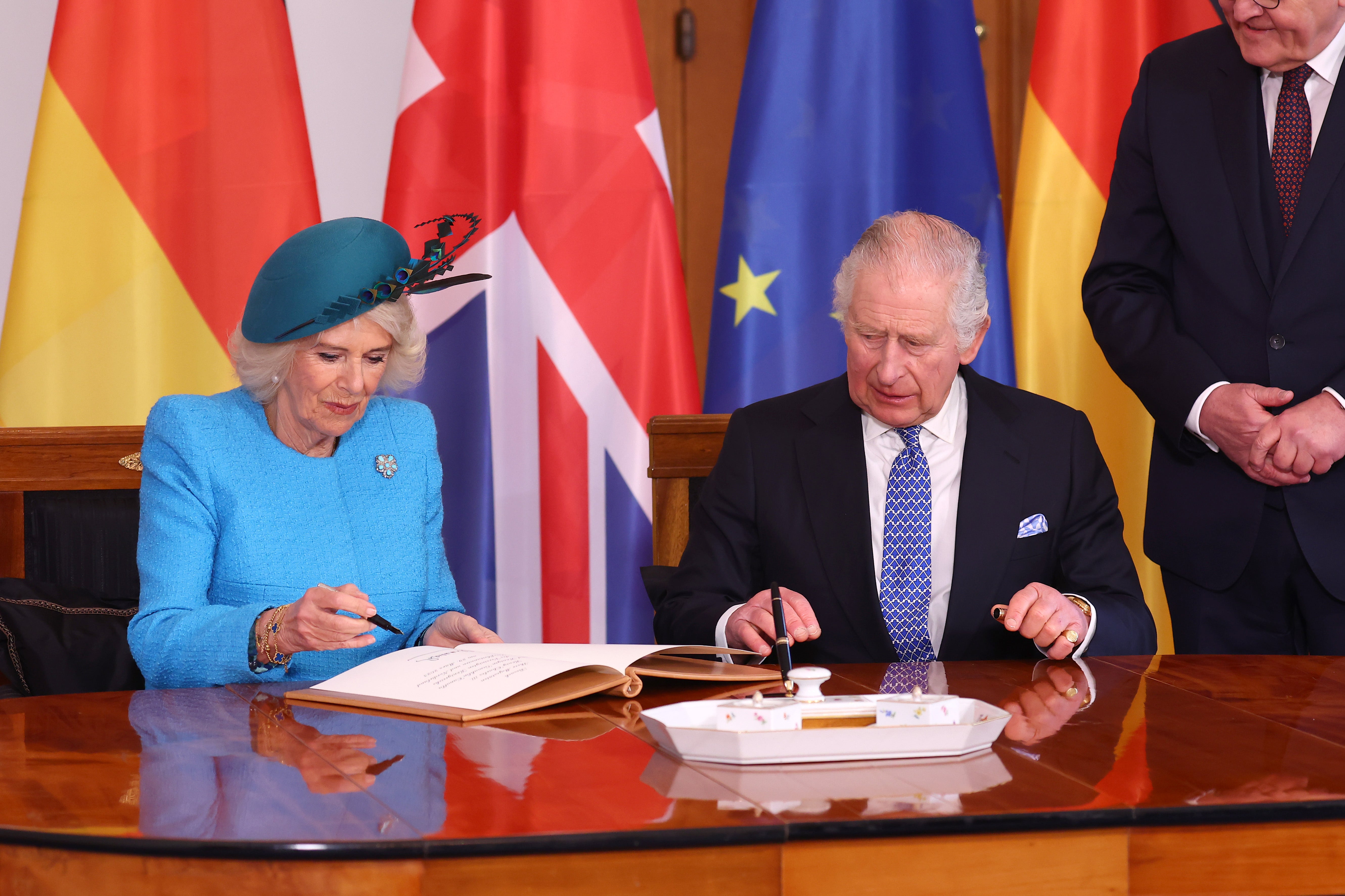 Camilla signs the official guest book as Charles looks on at the Schloss Bellevue presidential palace