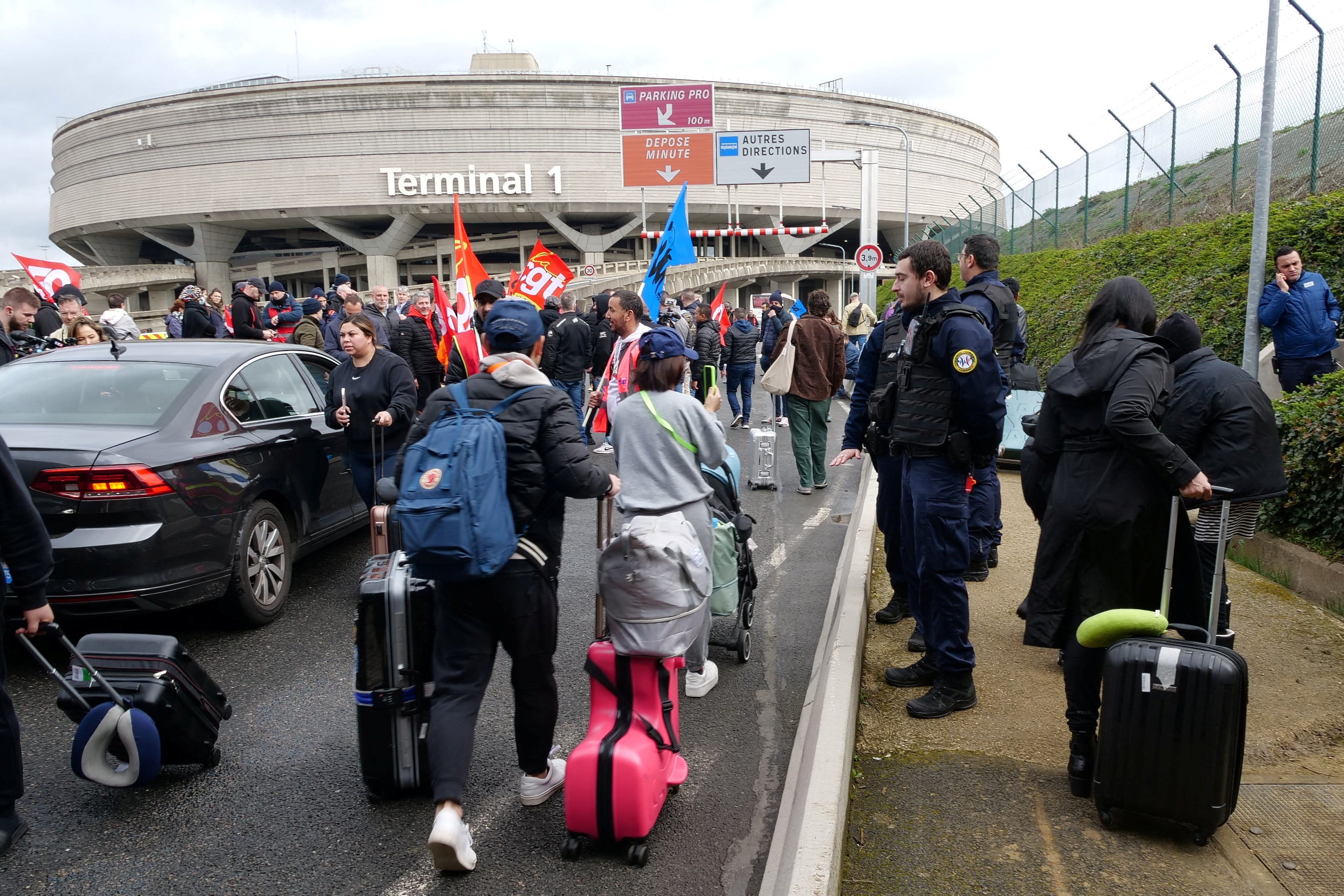 Passengers walk on the road with their luggage as airport workers on strike gather outside Paris-Charles de Gaulle airport in Roissy near Paris