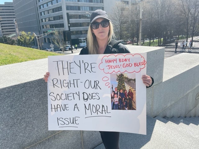 A 34-year-old Nashville mother holds up a poster featuring the Christmas card of Republican Rep. Andy Ogles, which depicts his family armed with weapons