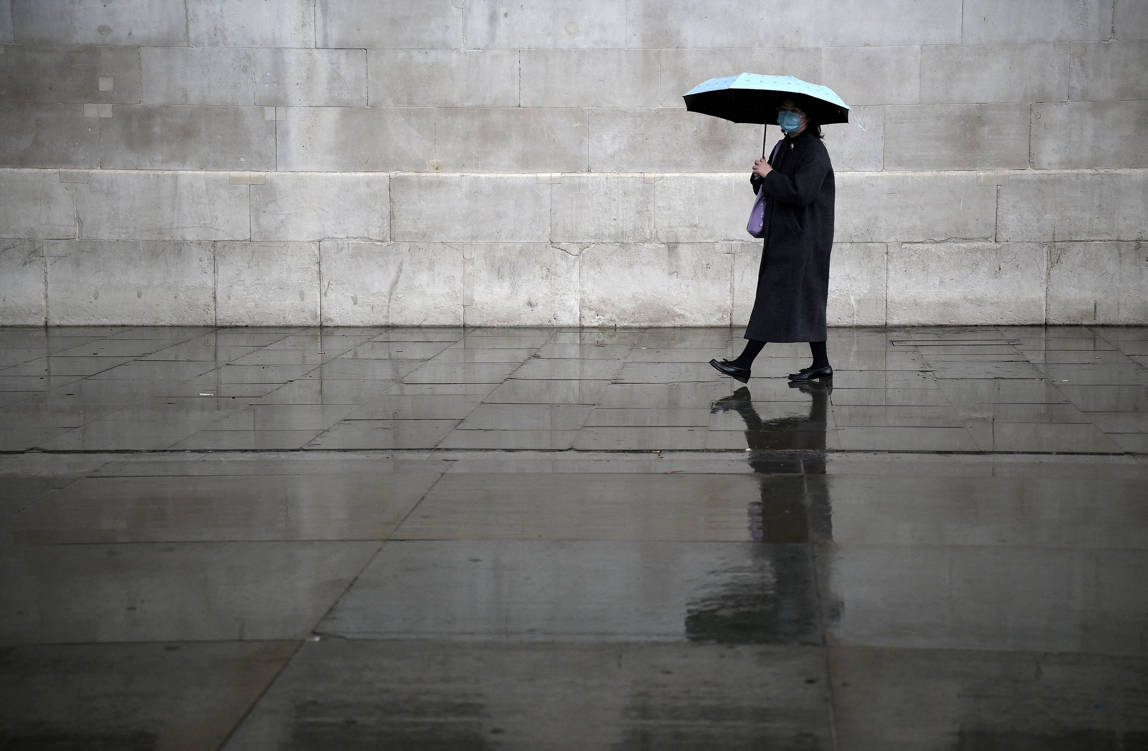 A pedestrian wearing a face covering shelters from the rain in central London