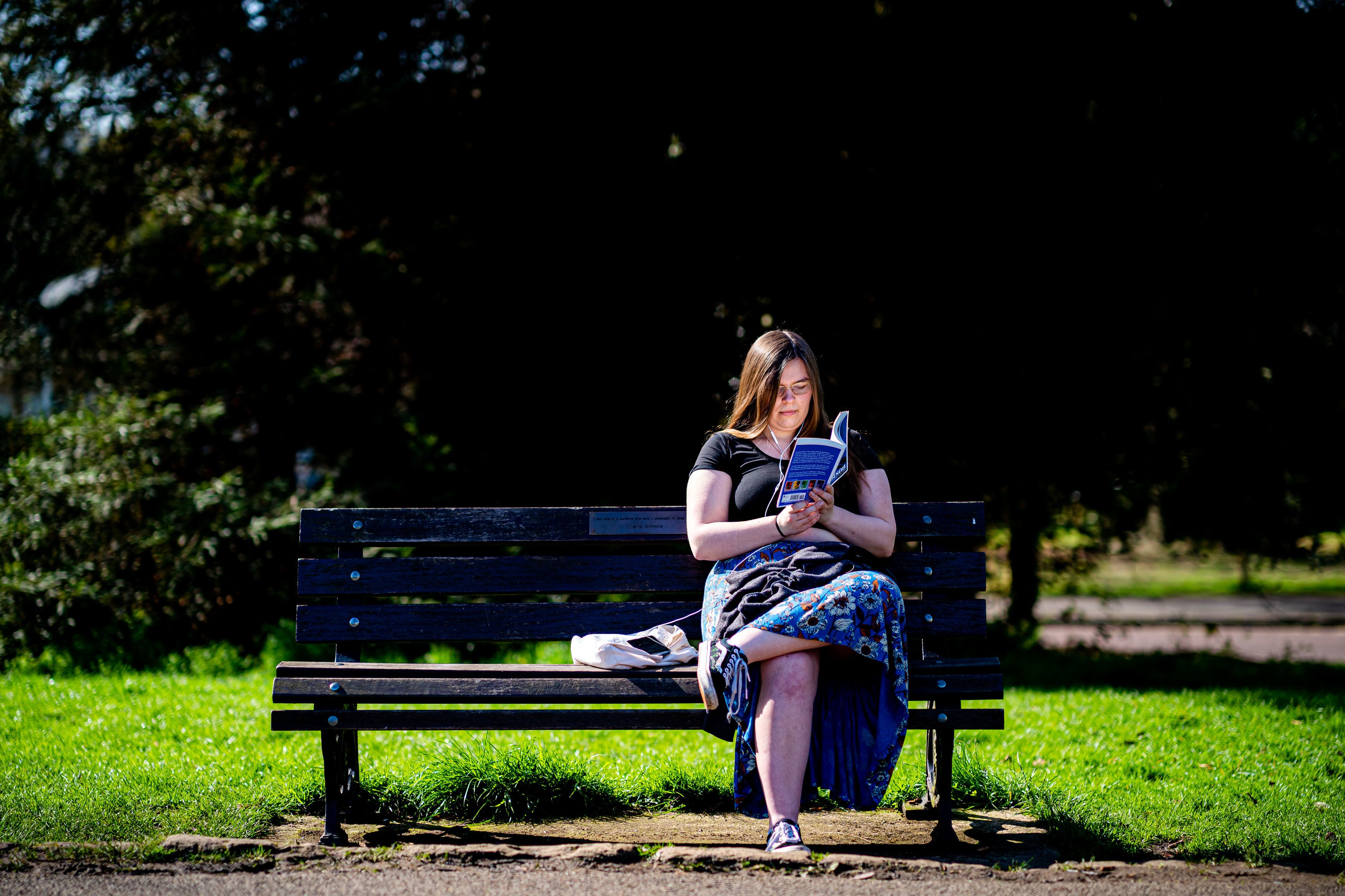 A woman reads a book on a park bench in the Royal Crescent, Bath