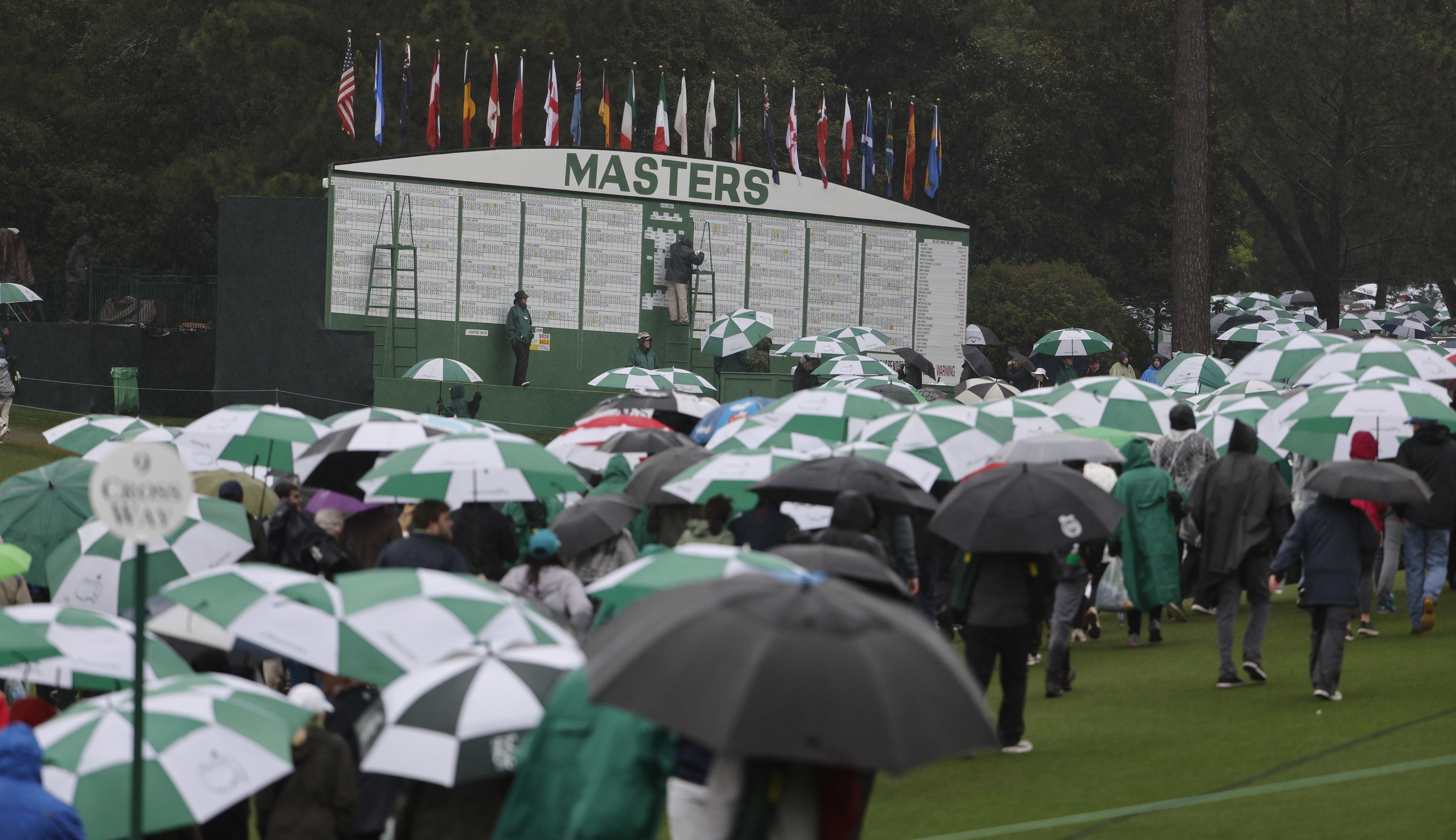 Patrons make their way past the leaderboard following the suspension of play in the third round of the Masters Tournament