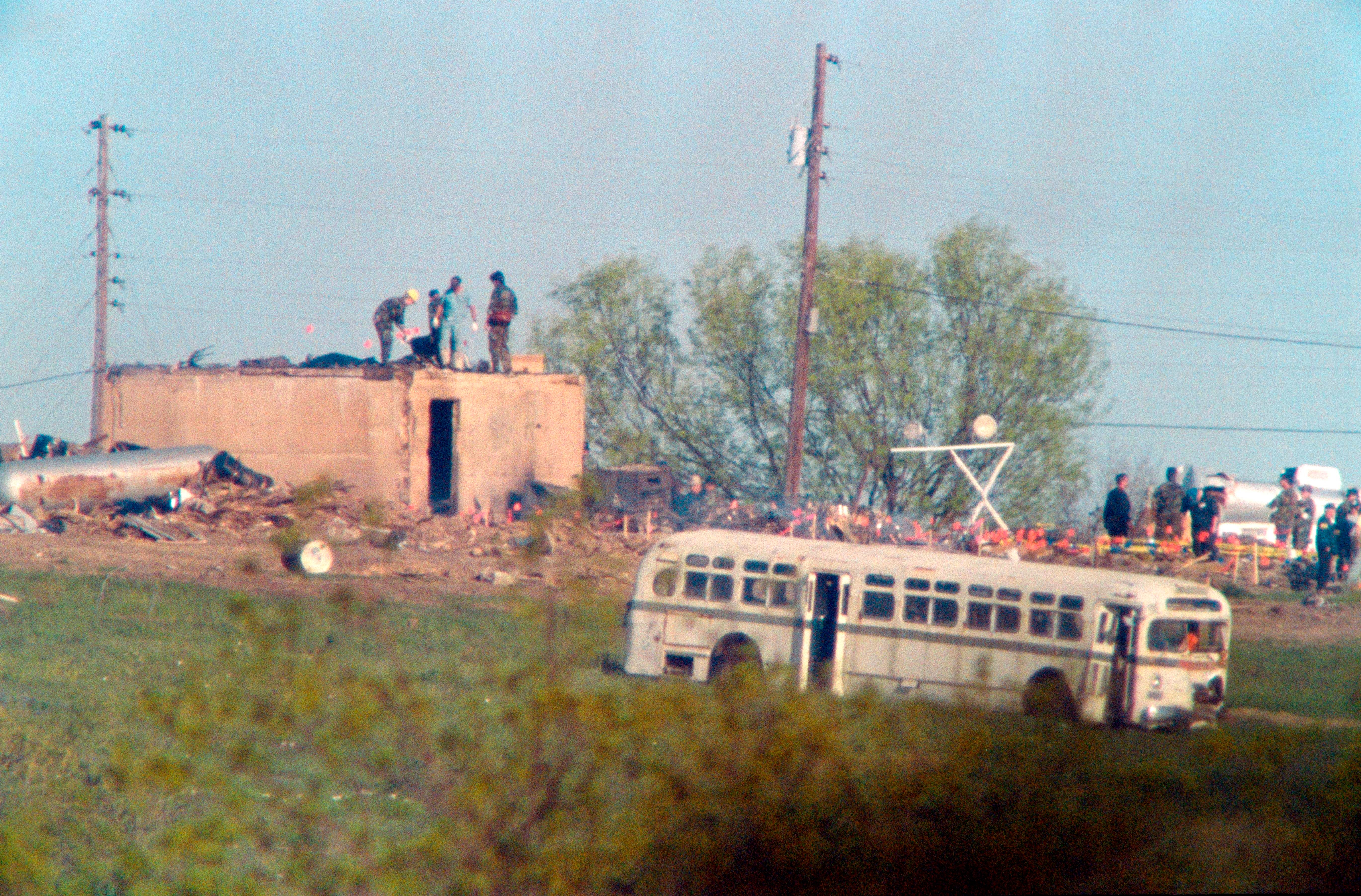 Texas Department of Safety Investigators and medical examiners search the rubble of the burnt-out compound and mark body locations with small flags