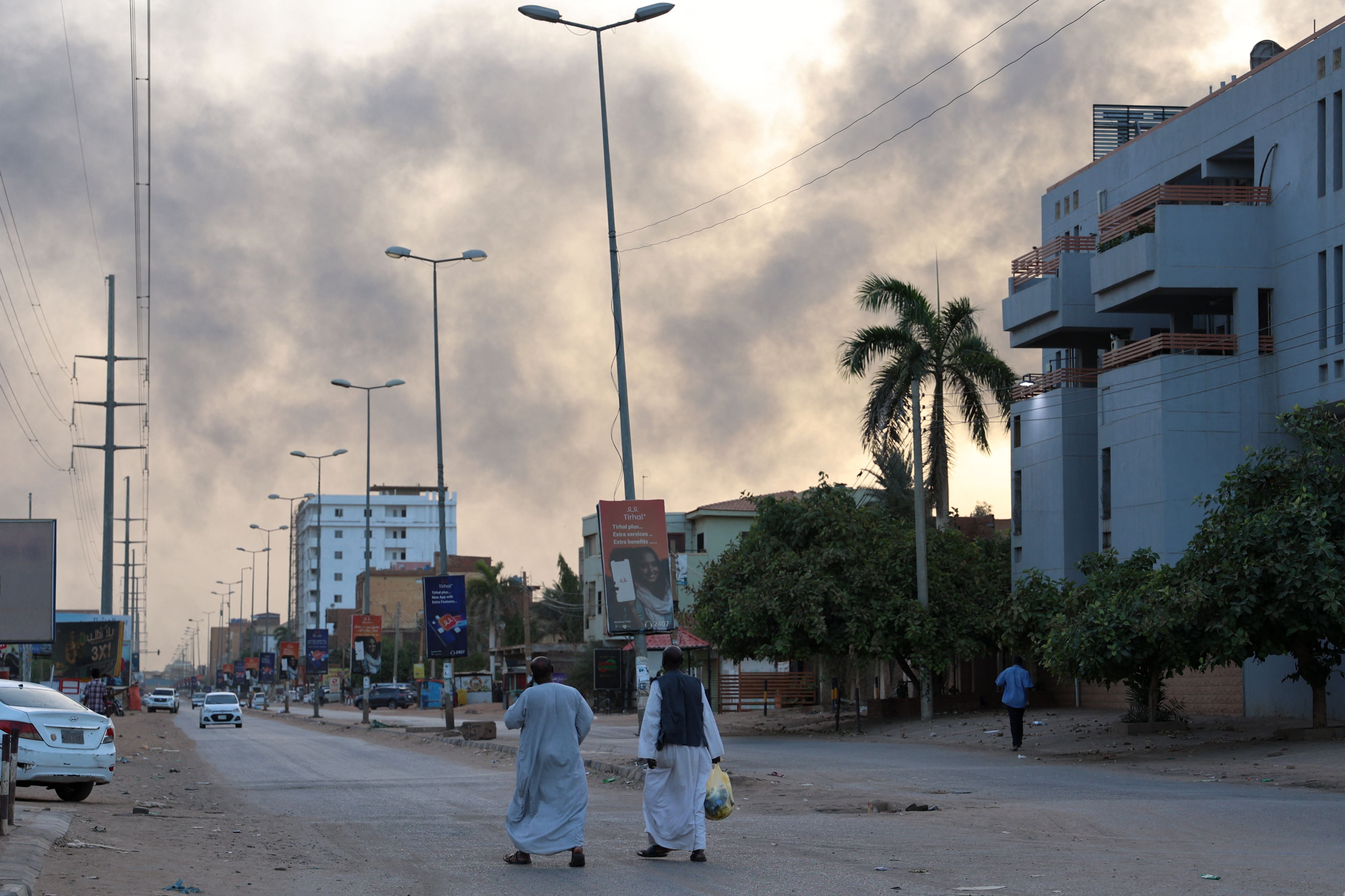 People walk along a street as smoke billows above residential buildings in east Khartoum