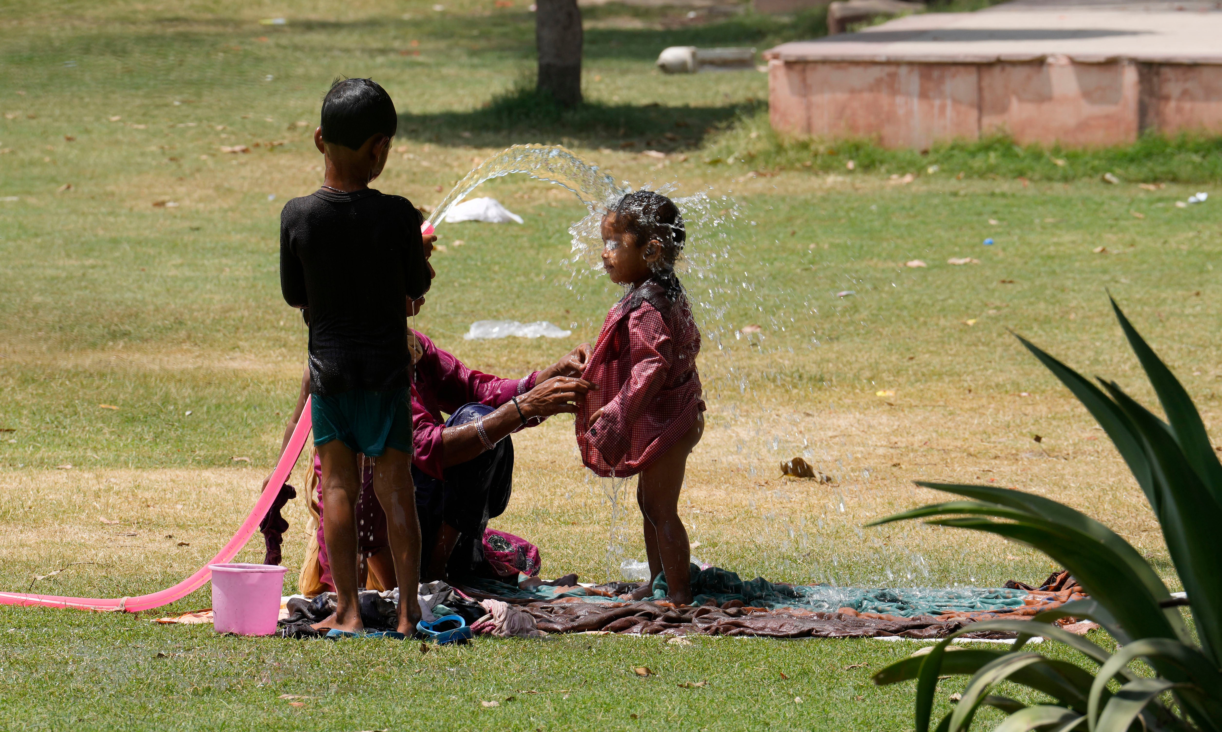 A family cools themself in a park using an irrigation water pipe as northern Indian continues to reel under intense heat wave in Lucknow, Uttar Pradesh on Wednesday, April 19, 2023