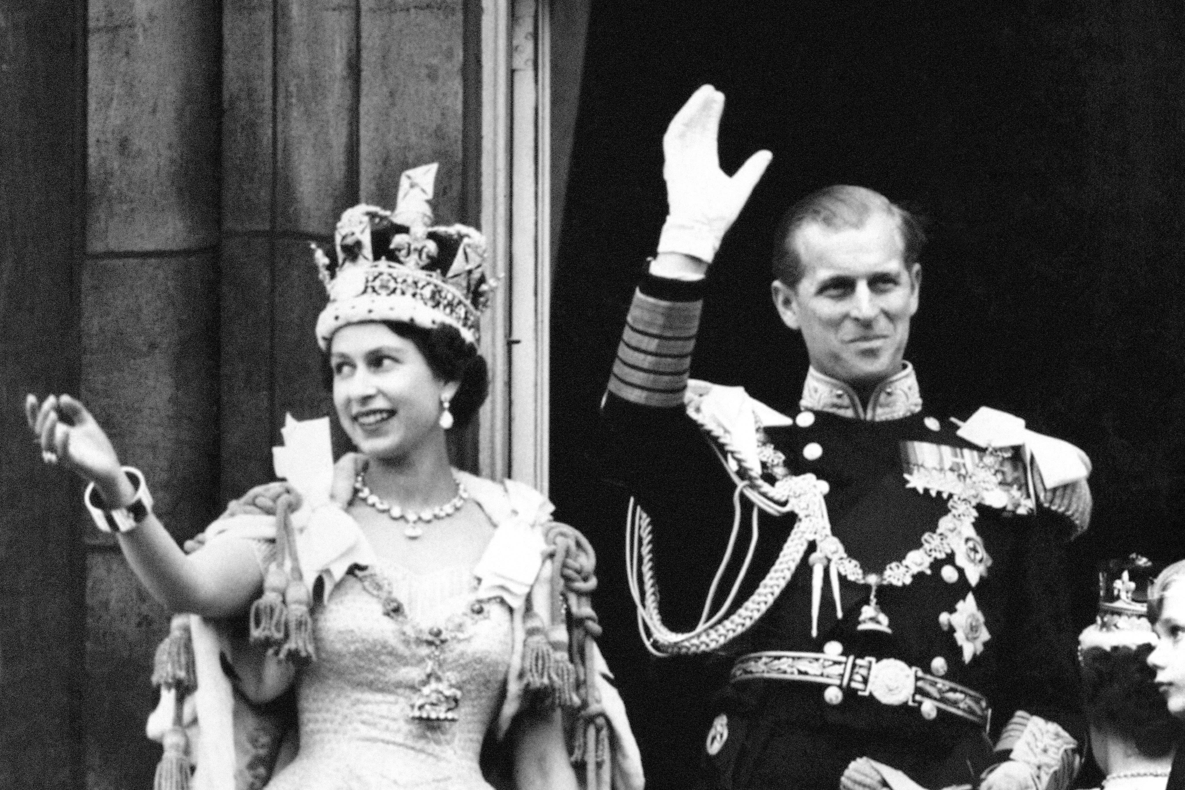 Queen Elizabeth II, wearing the Imperial State Crown, and the Duke of Edinburgh, dressed in uniform of Admiral of the Fleet, wave from the balcony at Buckingham Palace (PA)