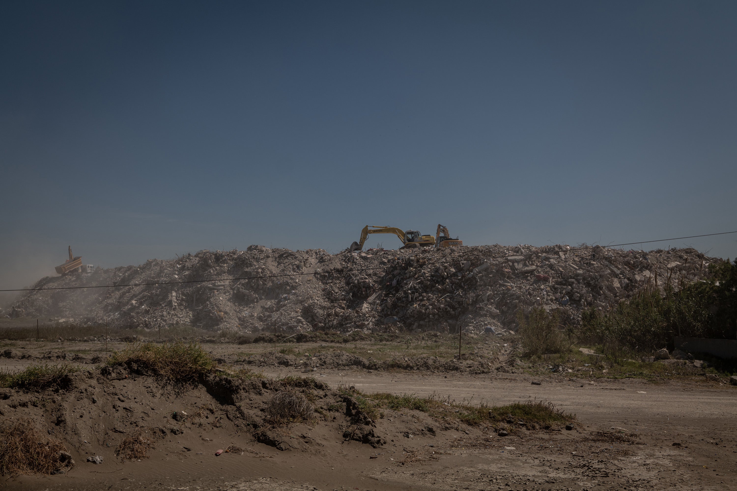 A dump truck and excavators sort through mass piles of rubble