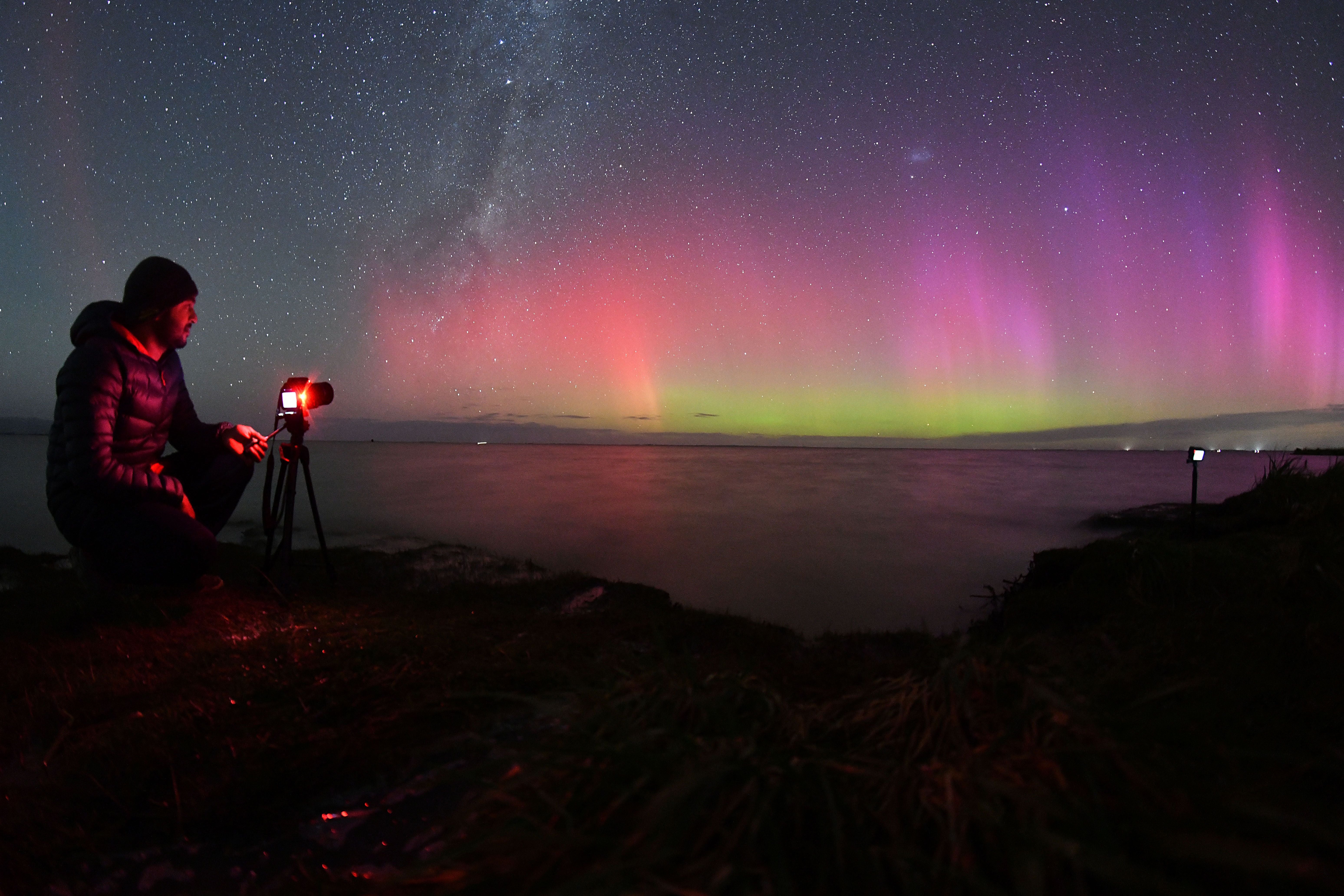 A photographer takes pictures of the Aurora Australis, also known as the Southern Lights, as it glows on the horizon over waters of Lake Ellesmere on the outskirts of Christchurch