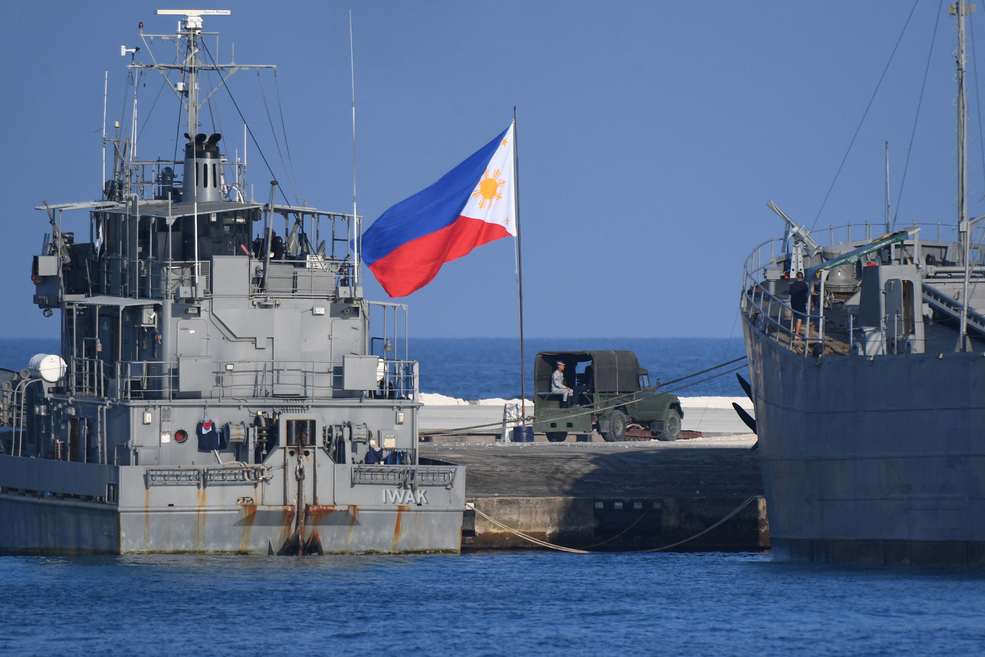 This photo taken on 21 April 2023 shows a Philippine flag fluttering next to navy ships anchored at the Philippine-occupied Thitu island in the disputed South China Sea