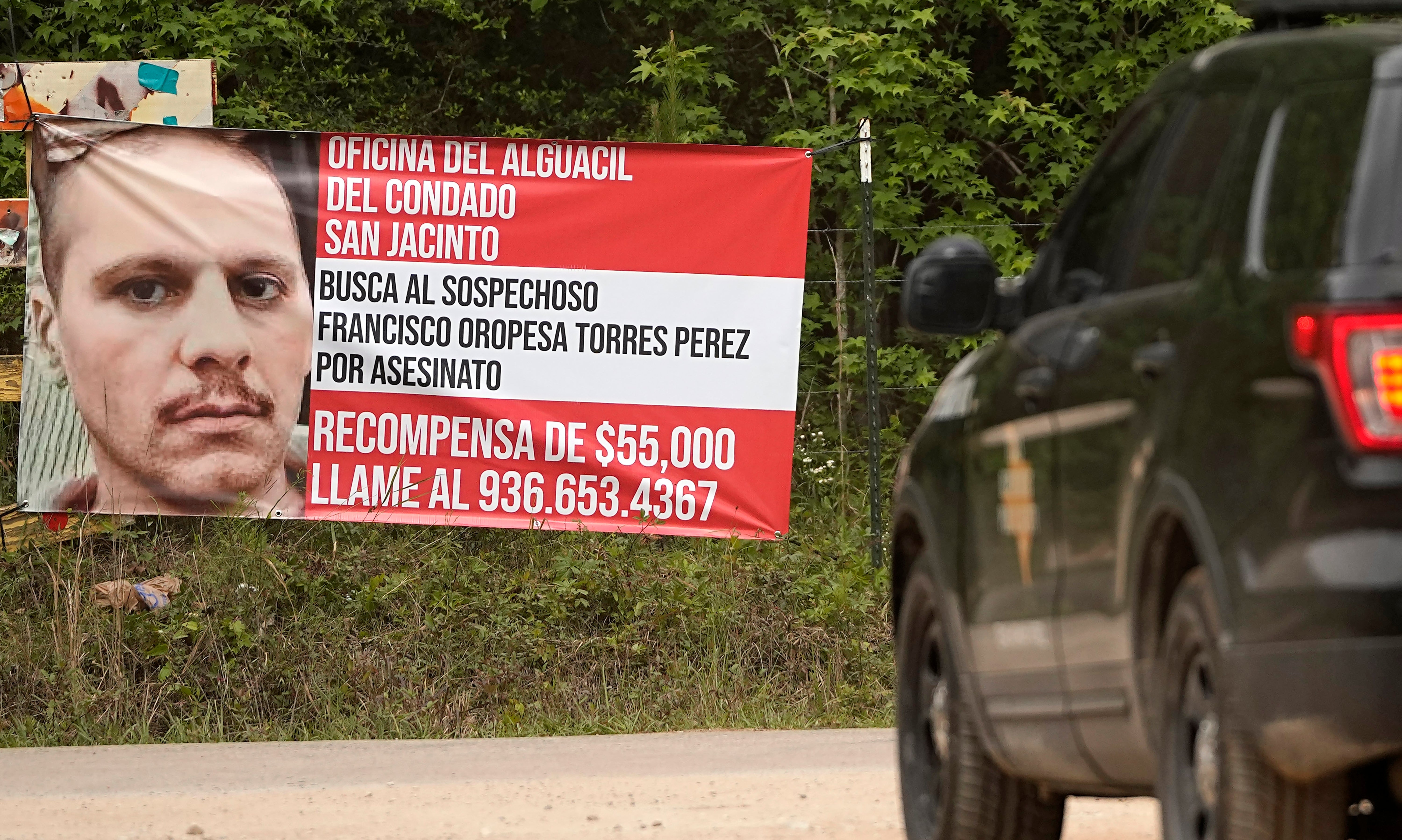 A state trooper vehicle passes a posted wanted sign for the mass shooting suspect