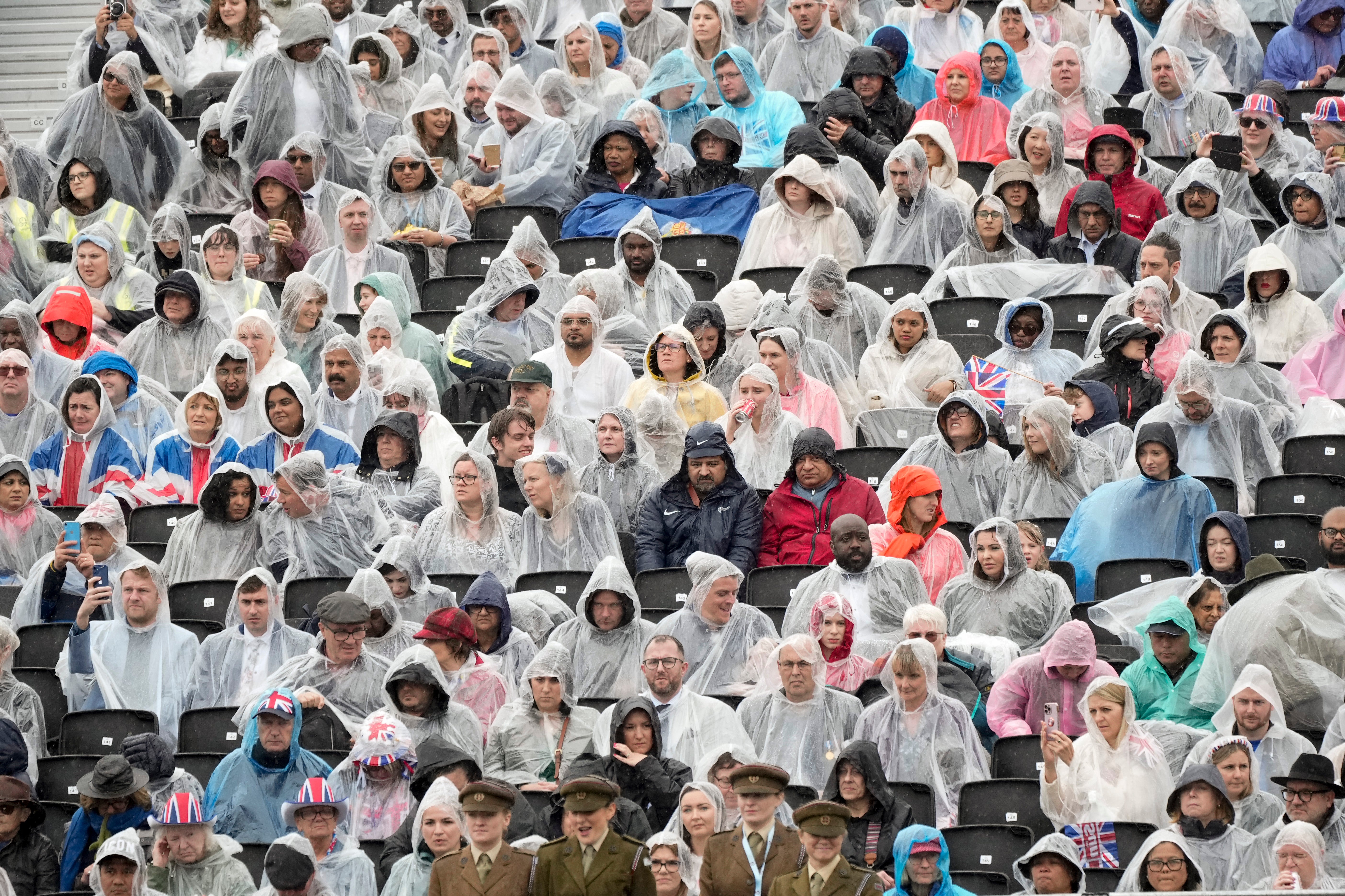 Rain soaked members of the public wearing ponchos wait for the King and Queen to pass by in procession