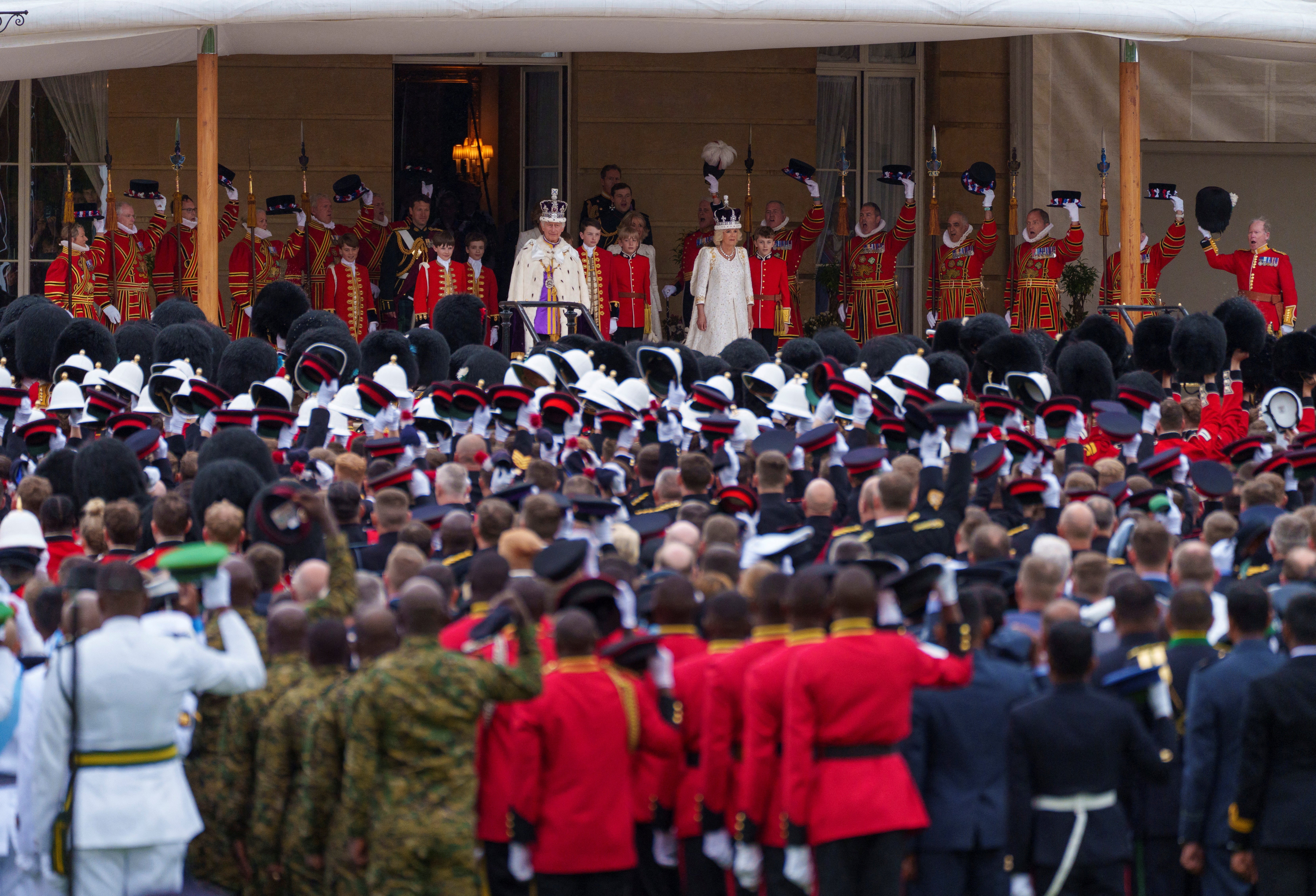 King Charles III and Queen Camilla receive the royal salute from gathered military personnel on the West Terrace of the Buckingham Palace gardens