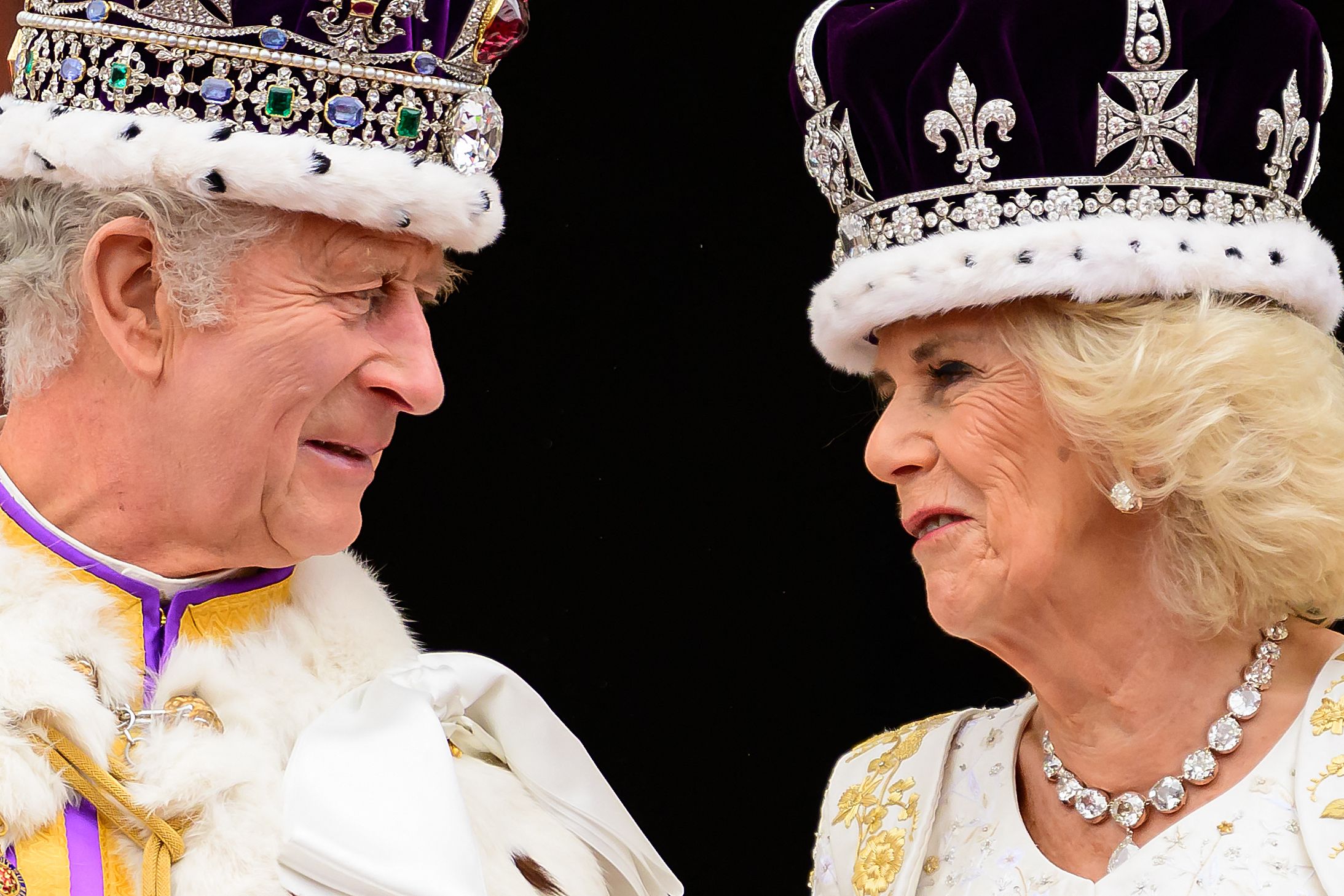 King Charles III looks at Queen Camilla as they stand on the Buckingham Palace balcony