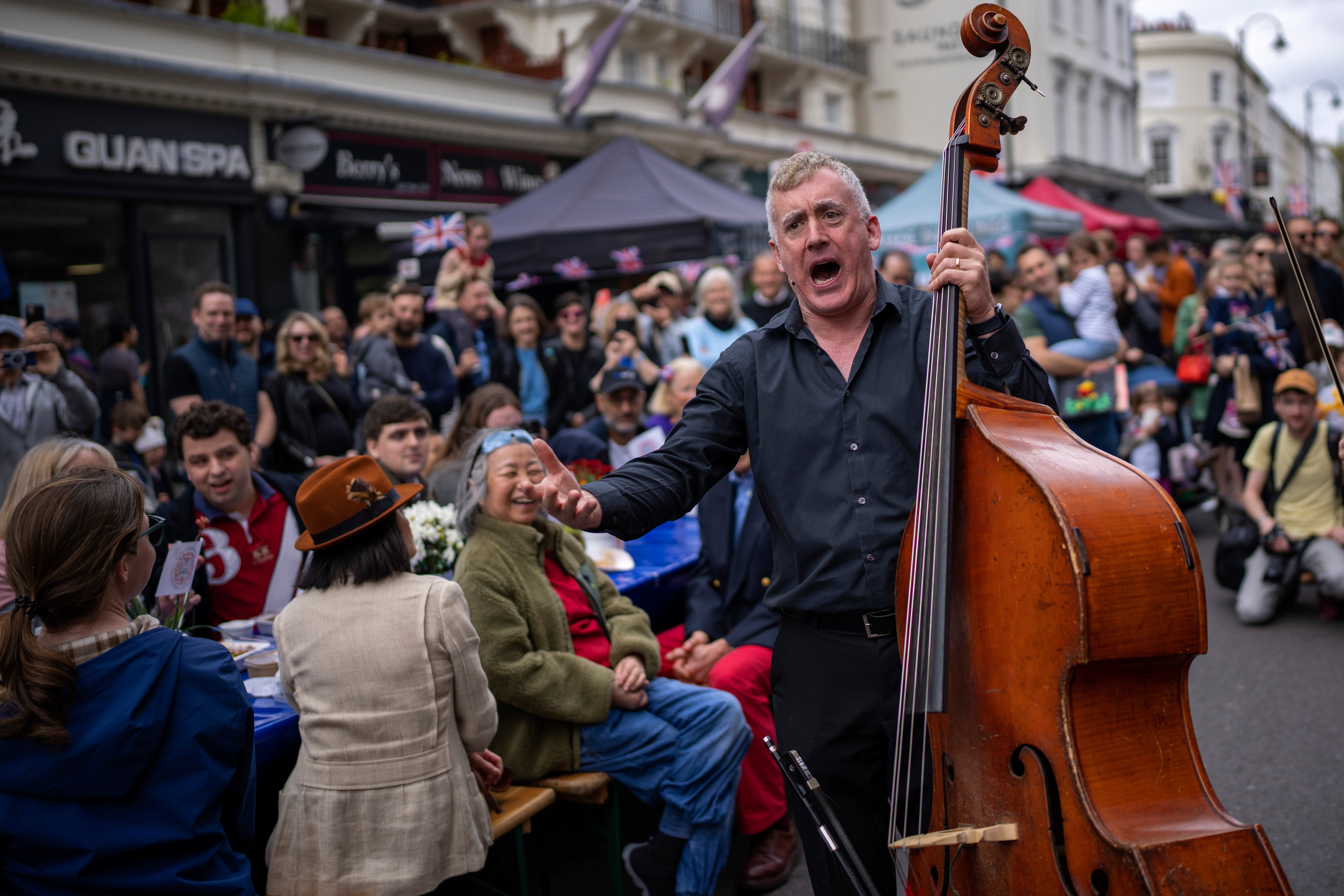 Musicians play their instruments as people sit at long tables to eat their lunch in London