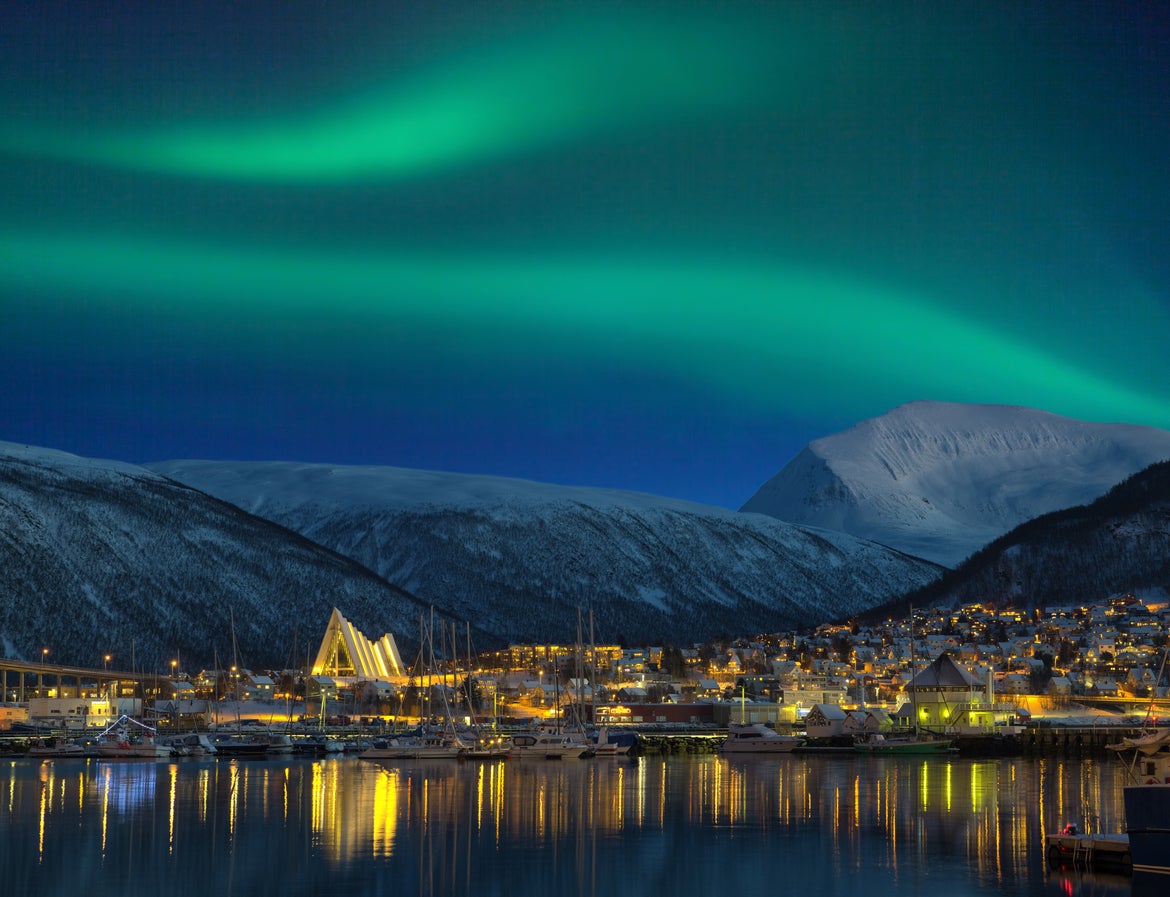 A view of an illuminated Tromso with the Northern Lights over the city