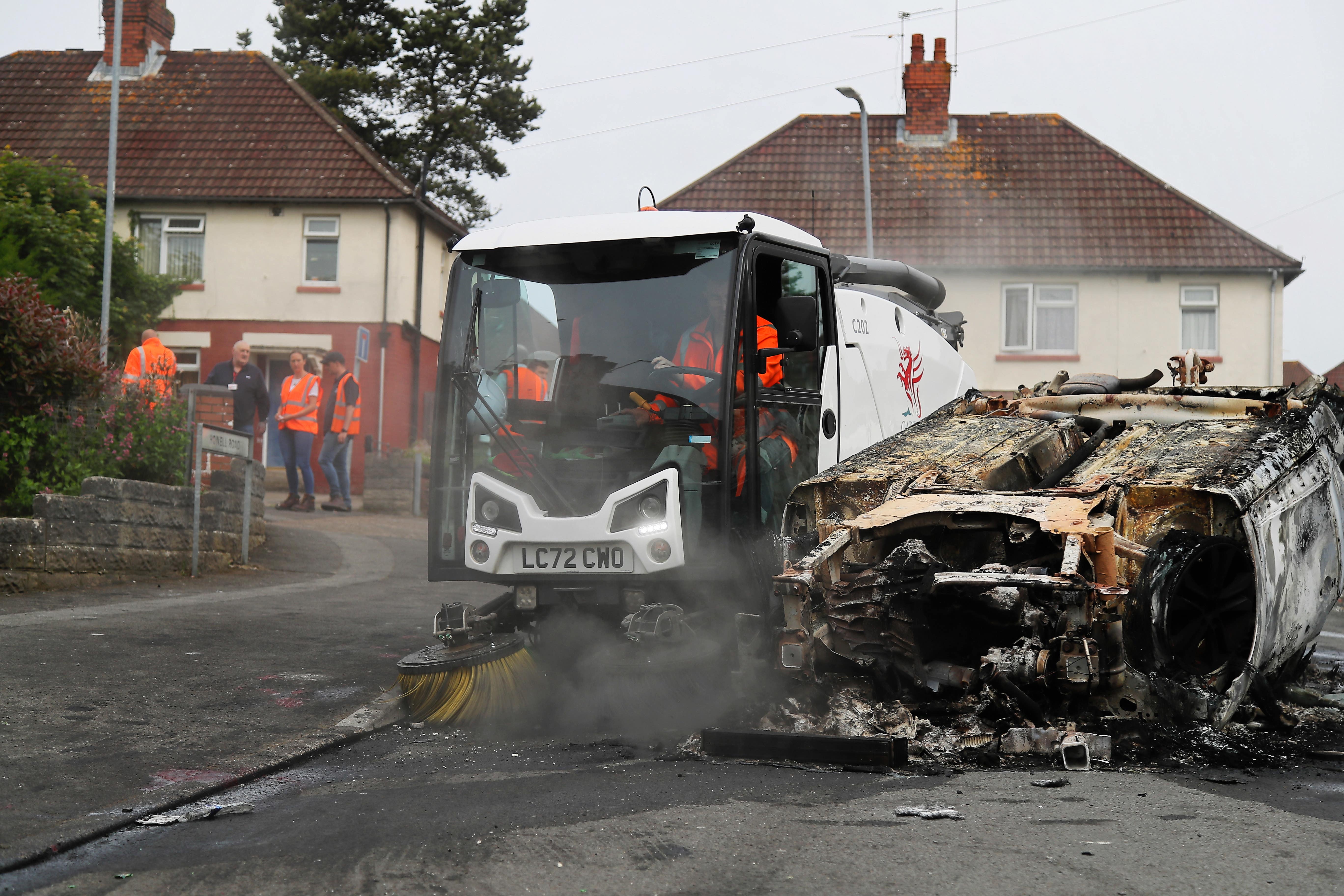 Council workers cleared debris from the area around a car that was set alight in the riot