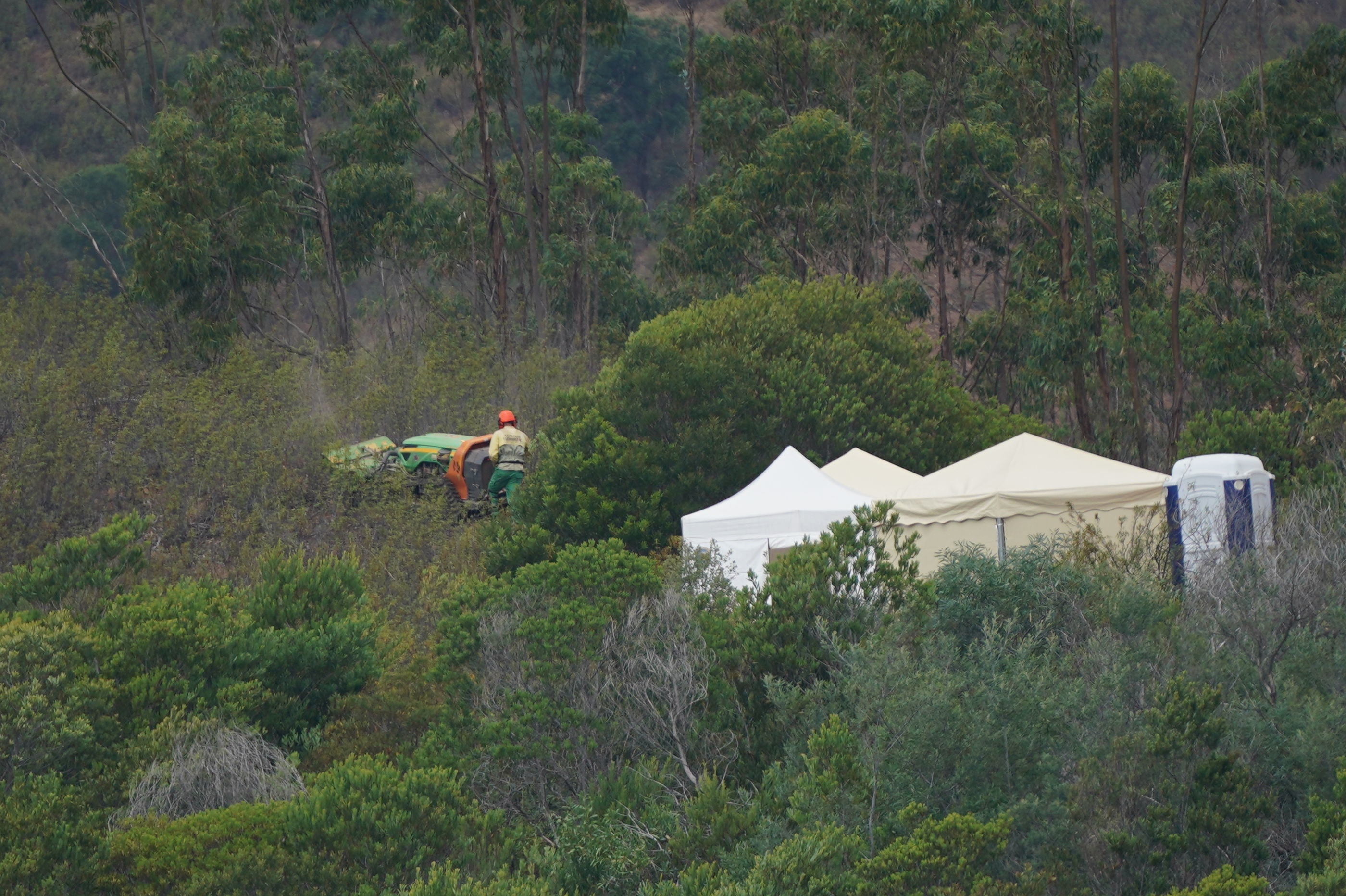 Personnel clear undergrowth with machinery at Barragem do Arade reservoir close to white tents