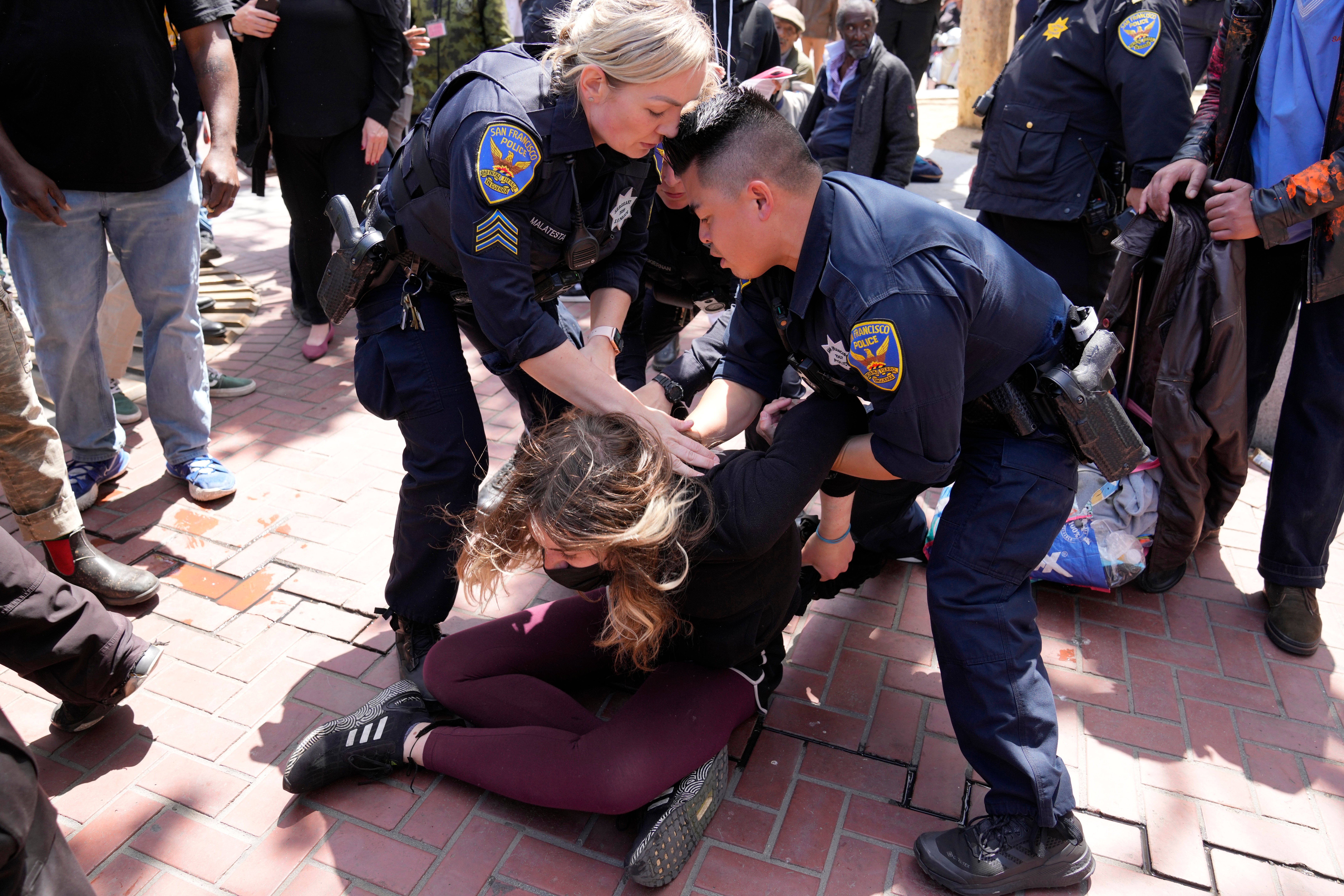 A protester who threw a brick at a color guard after a rare outdoor meeting of the Board of Supervisors is restrained by police at UN Plaza in San Francisco, Tuesday, May 23, 2023.