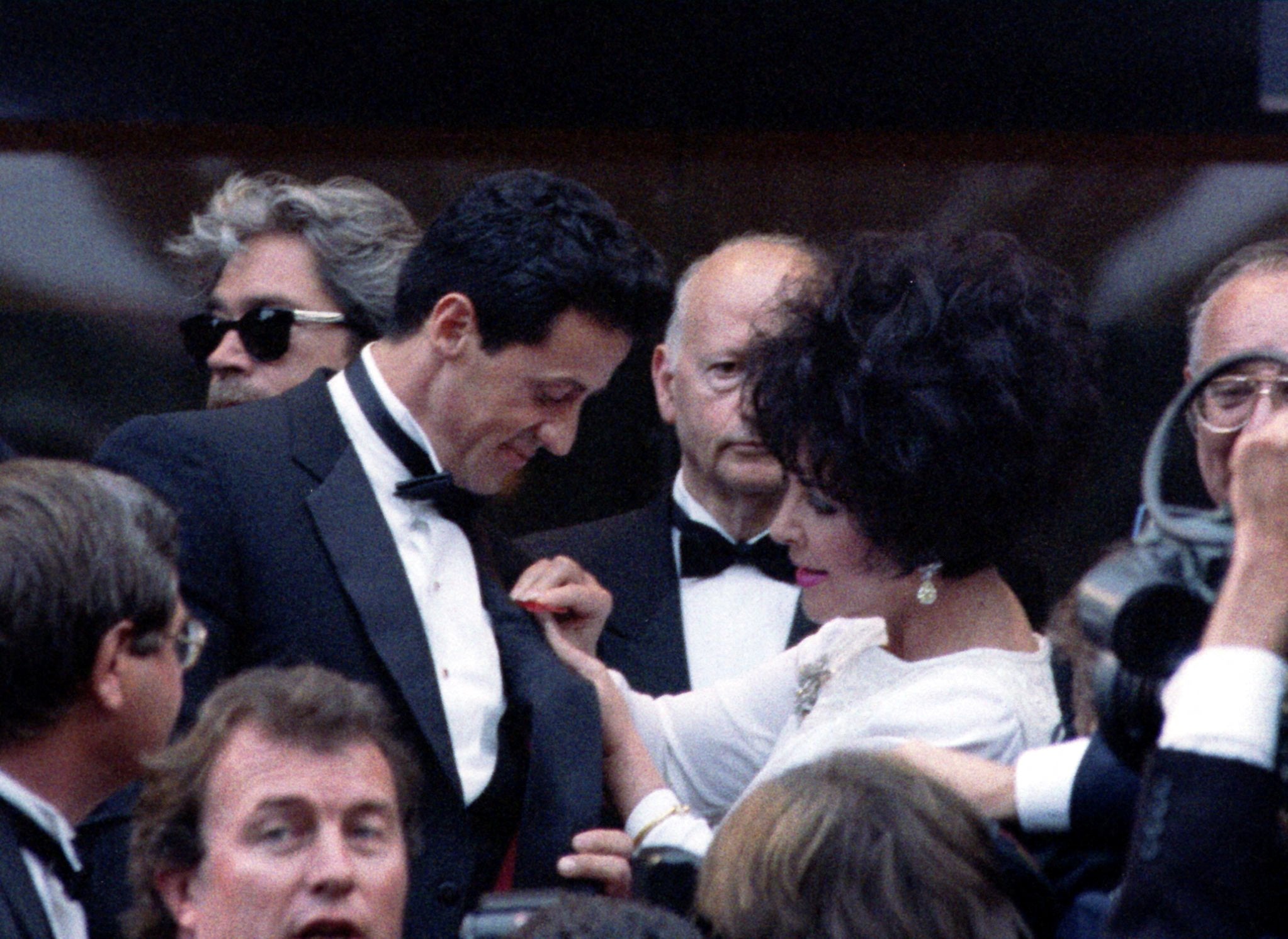 Elizabeth Taylor pins a red ribbon on Sylvester Stallone's tuxedo during the Cinema for Aids evening at the 46th Cannes on 20 May 1993