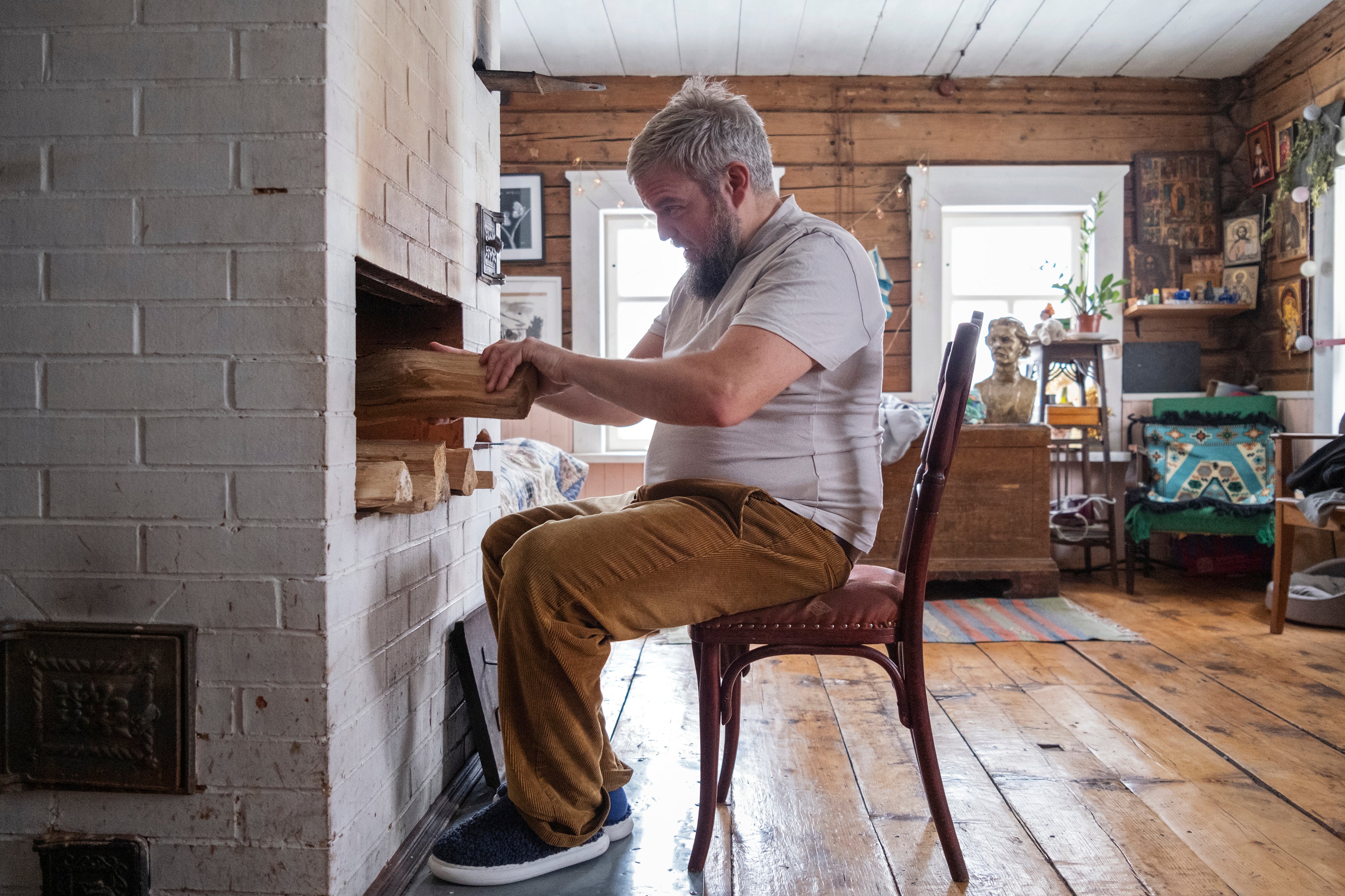 Akimov adds wood to the fire in a traditional Russian pechka stove