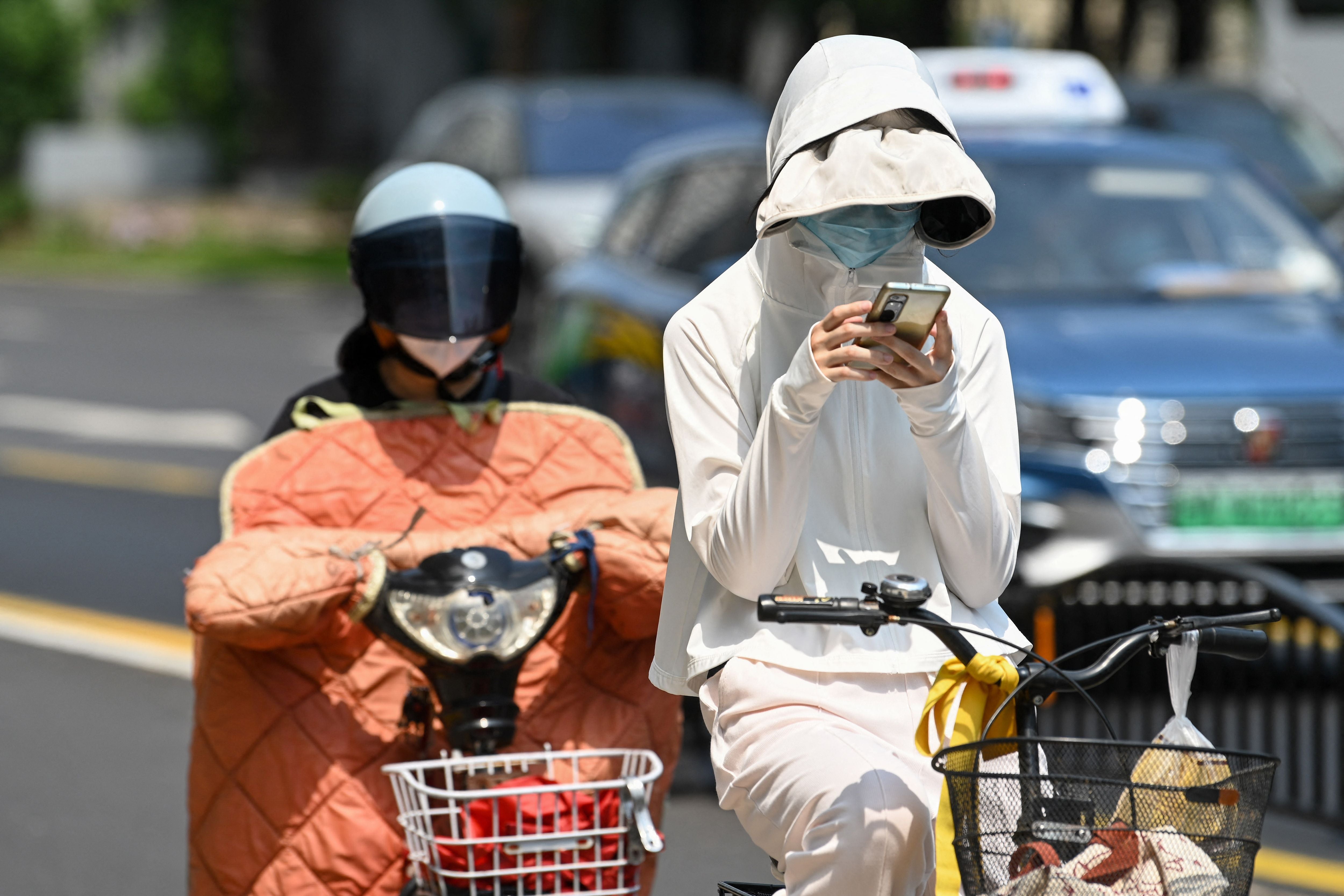 A woman wearing sun protective clothing commutes on a bicycle amid hot weather in Shanghai on Monday