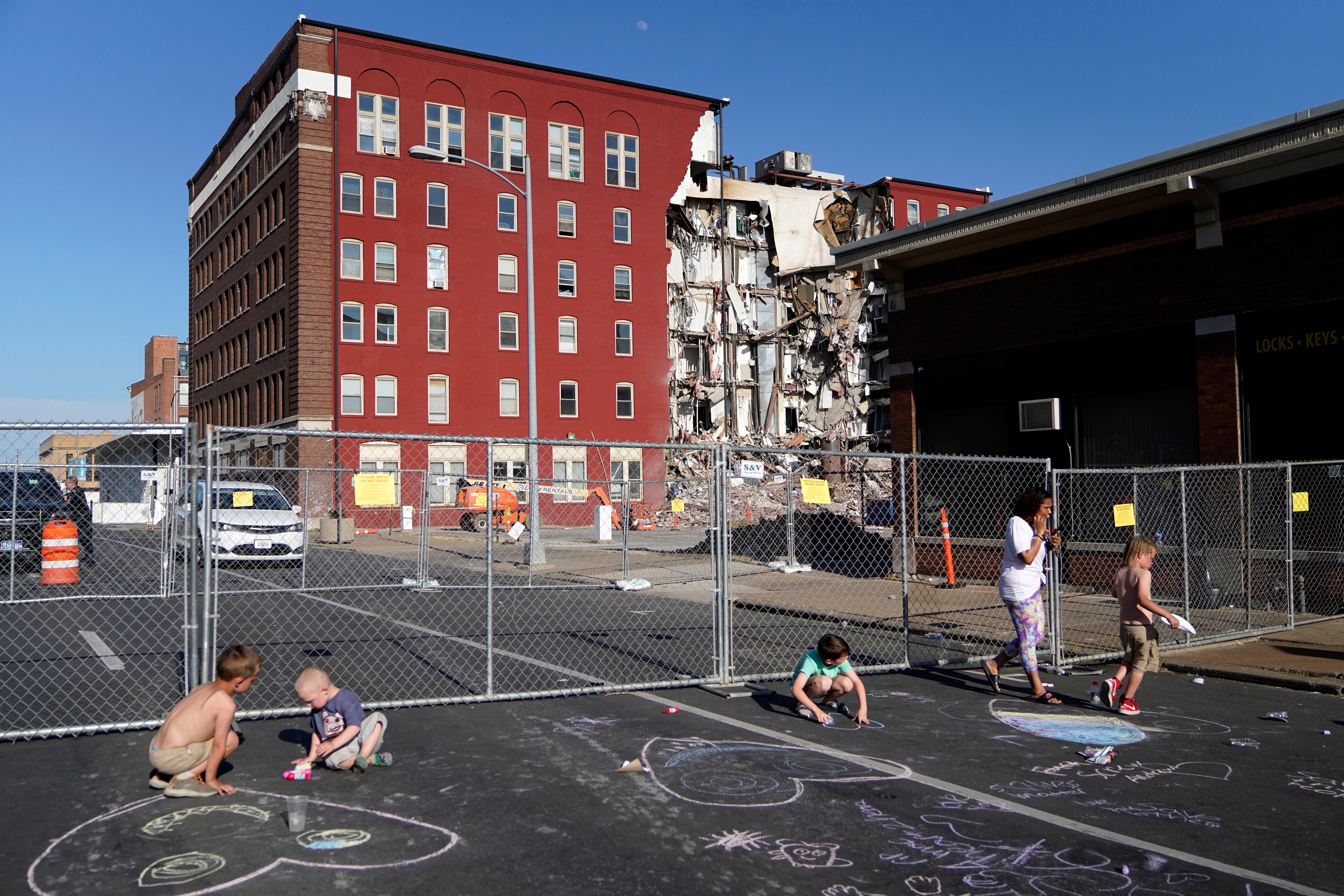 Children draw on the ground with chalk at the scene where an apartment building partially collapsed on Sunday afternoon