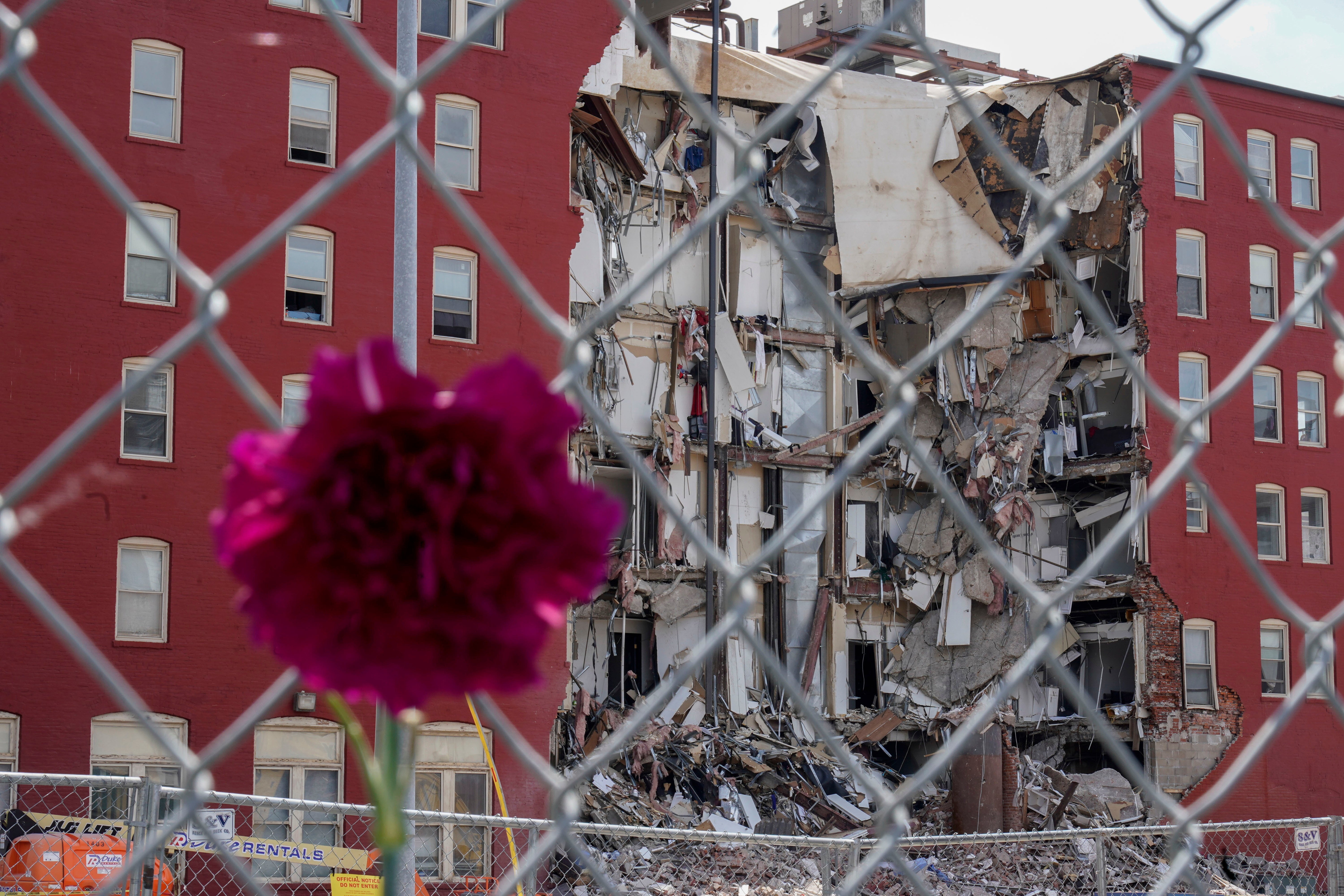 A flower hangs from a fence at the where on Sunday an apartment building partially collapsed in Davenport, Iow