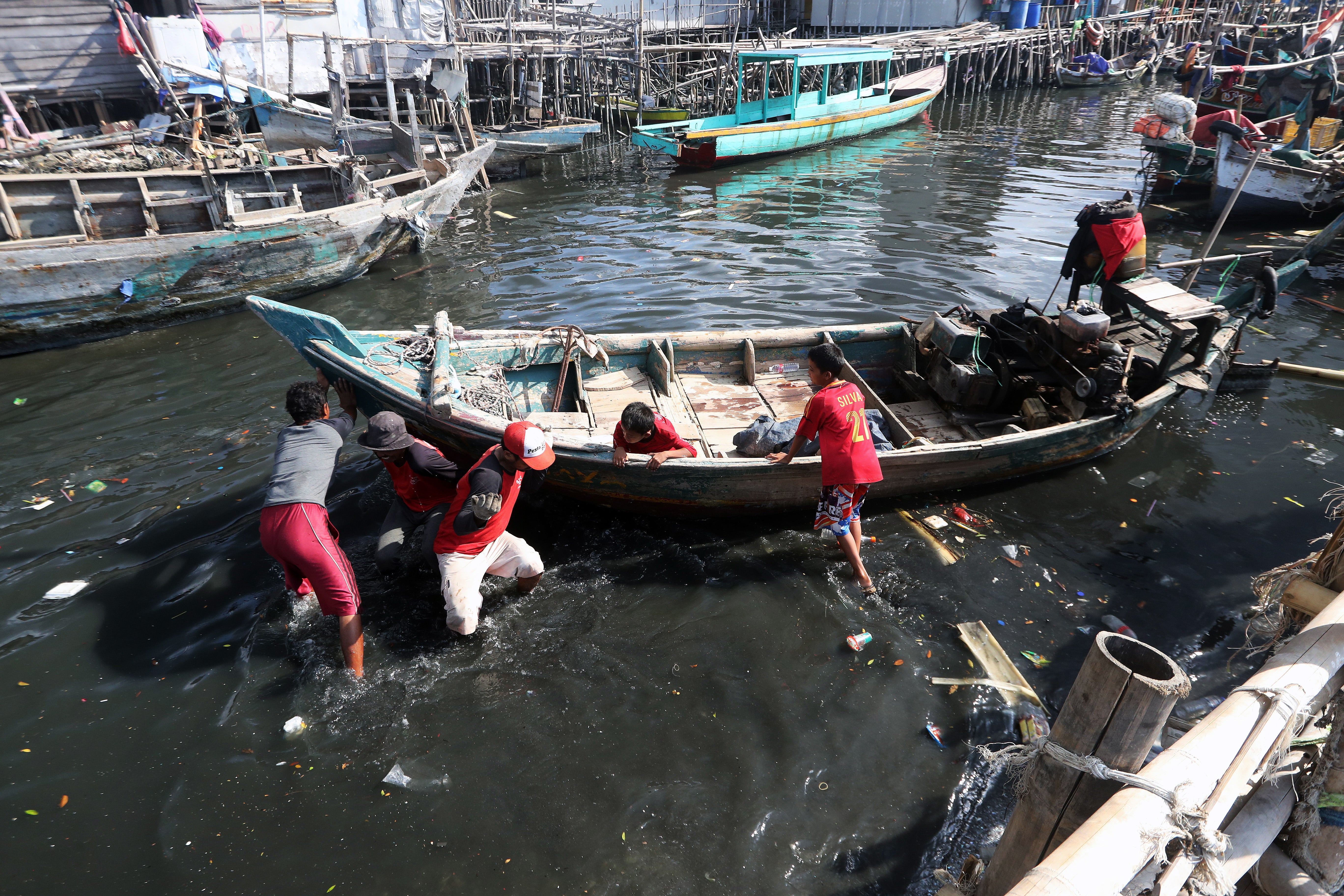 Fishermen push their wooden boats which have run aground in the shallow harbor