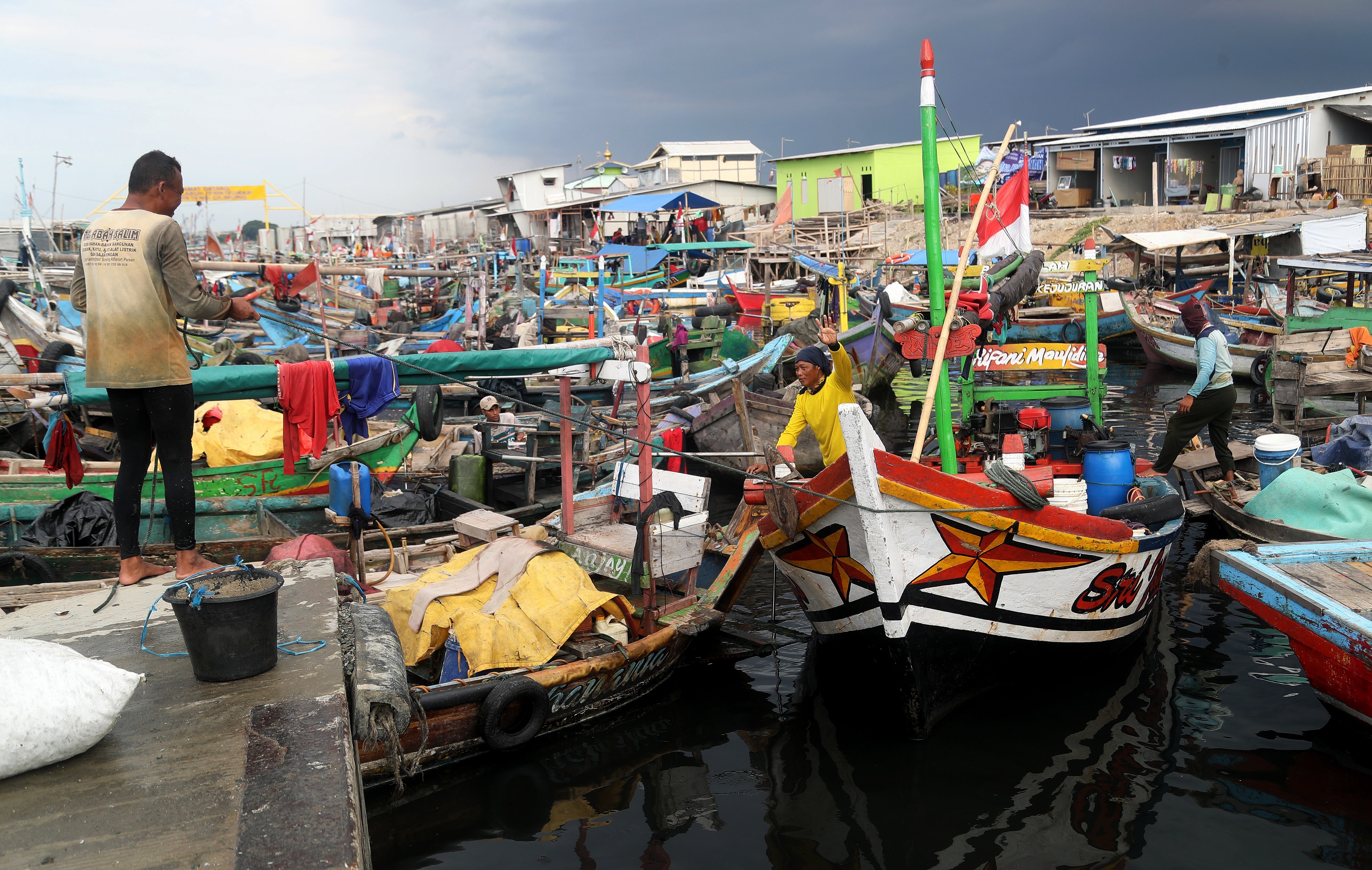 Fishermen manoeuvre their boats at a fishing dock behind the coastal embankment in Cilincing, Jakarta