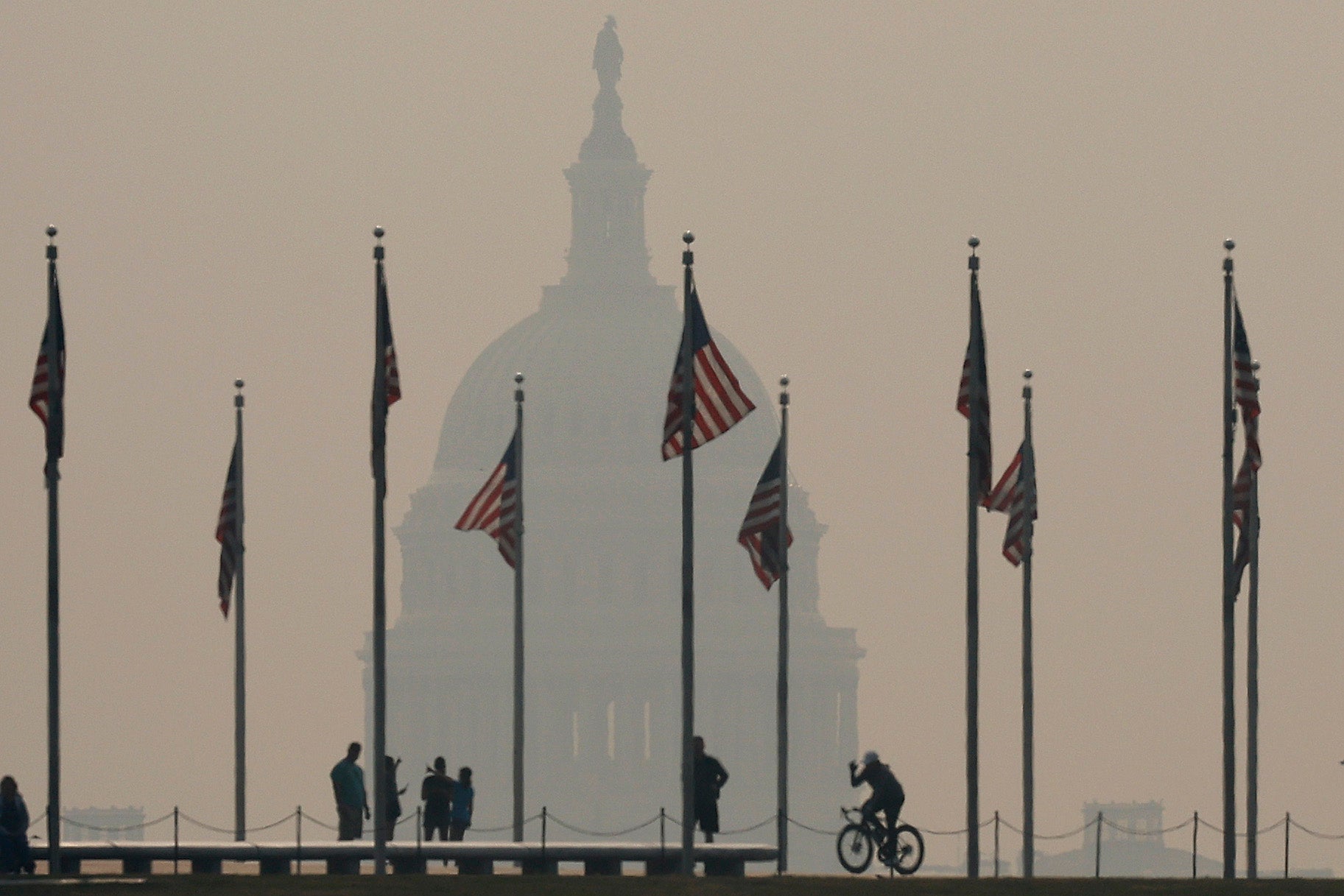 Tourists walk around the base of the Washington Monument as wildfire smoke casts a haze of the US Capitol on the National Mall on June 07, 2023 in Washington, DC