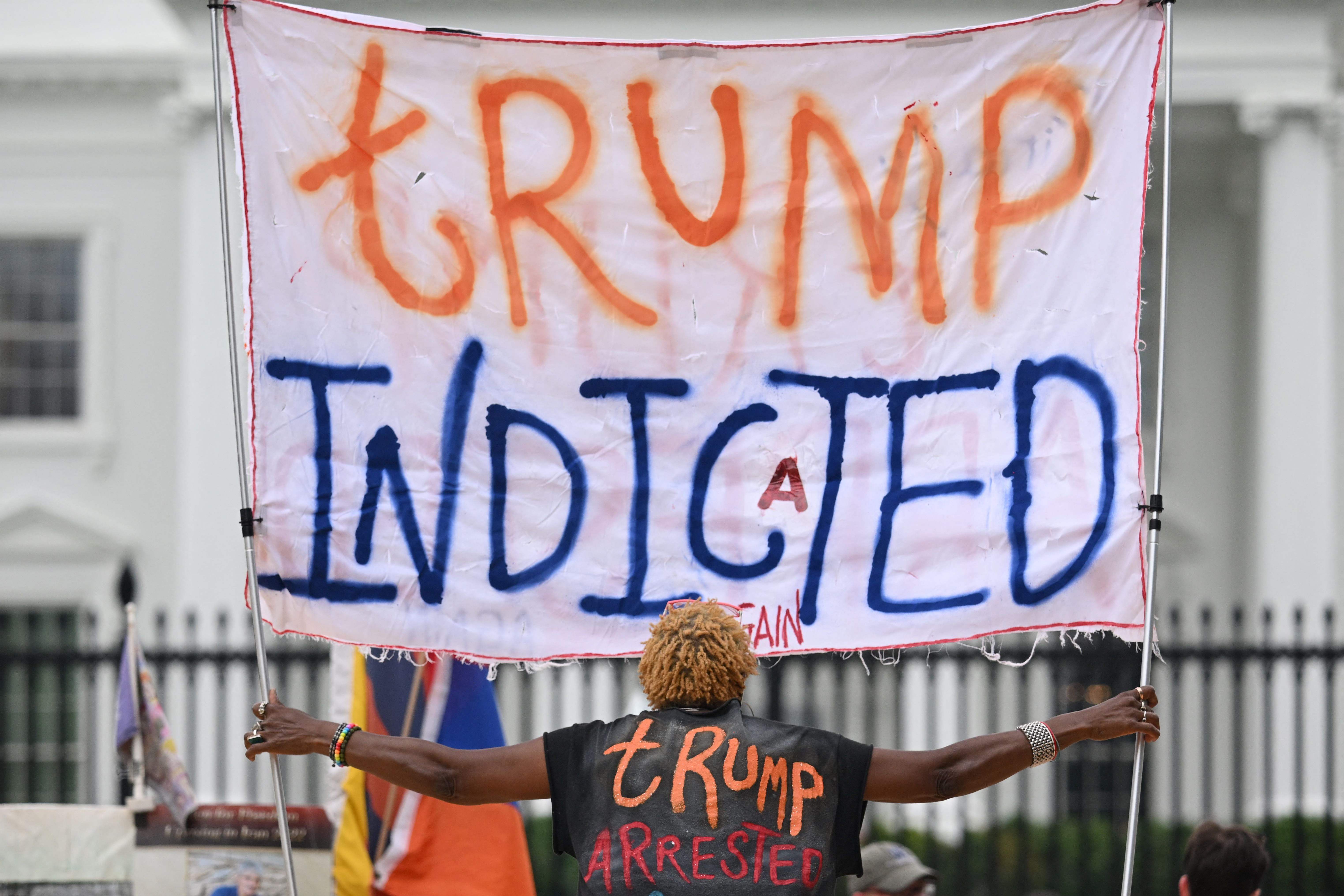 A person celebrating the indictment of former US president Donald Trump holds a banner in front of the White House