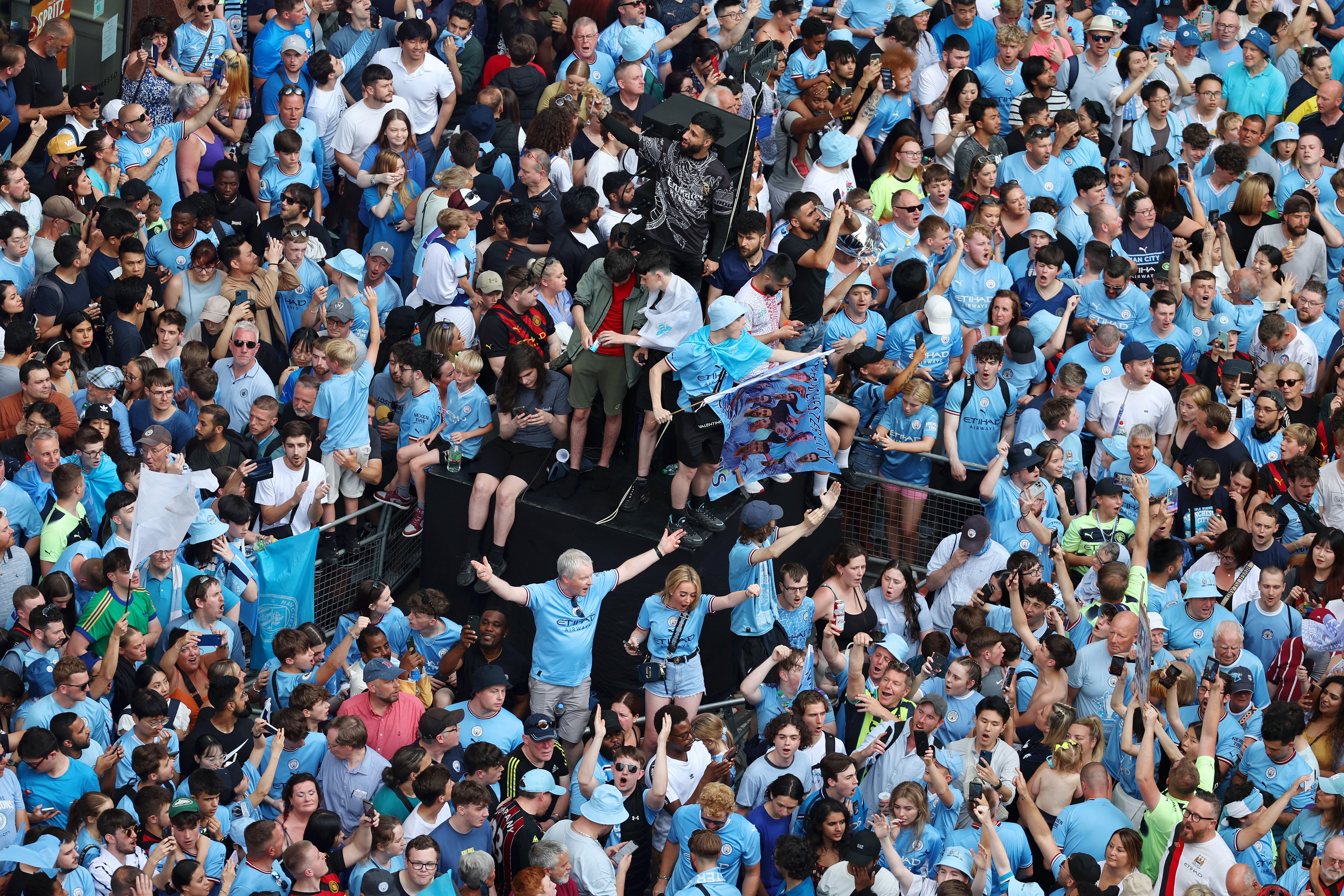 Manchester City fans take shelter from the rain ahead of the Treble Parade in Manchester.