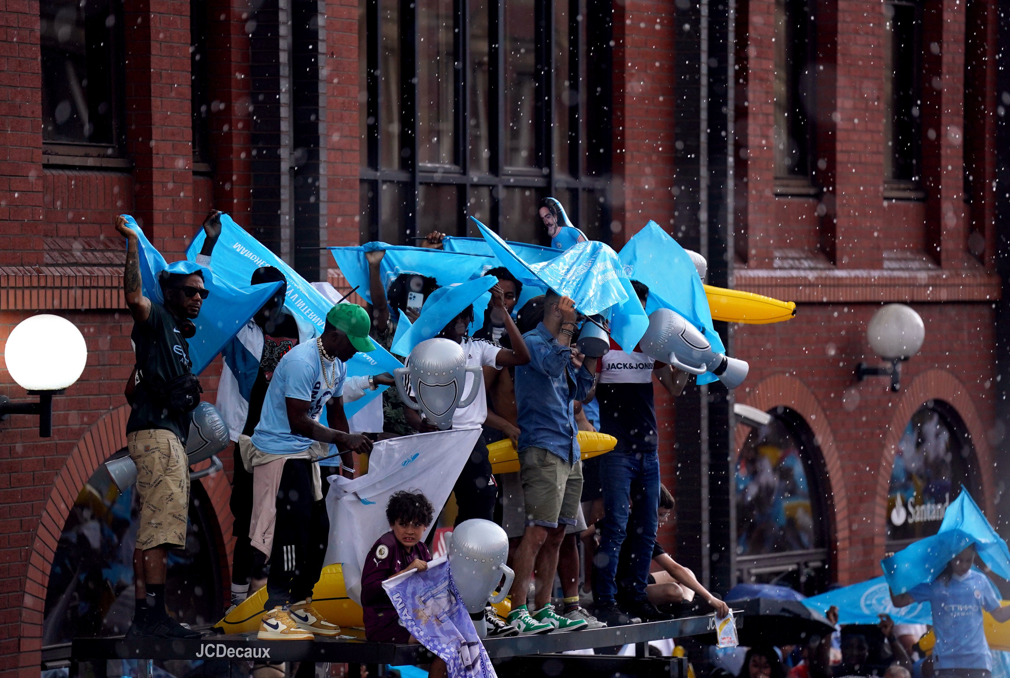 Manchester City fans take shelter from the rain ahead of the Treble Parade in Manchester.