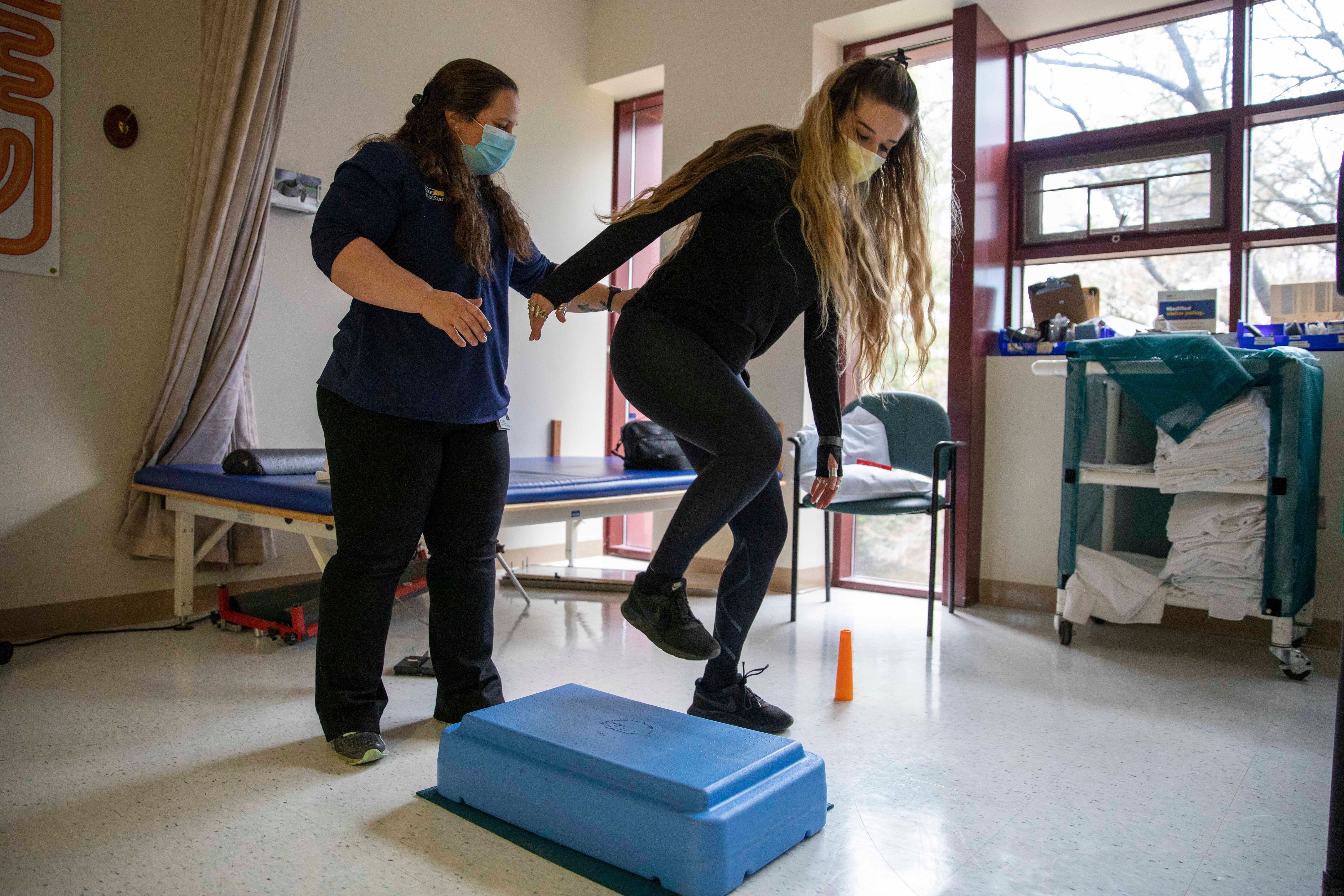 A physical therapist supports Amber as she does a balance and coordination exercise