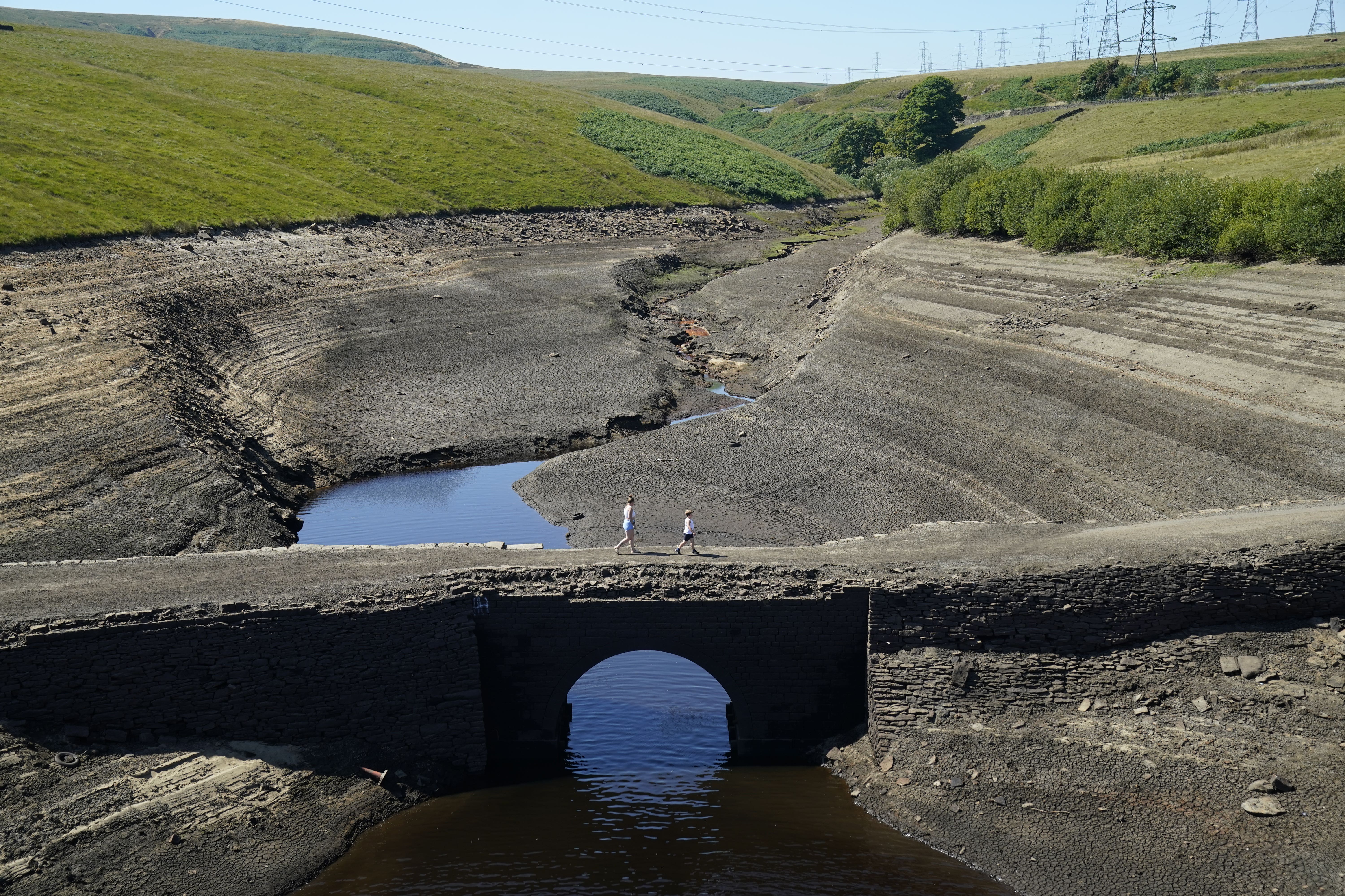 People walk across the dry cracked earth at Baitings Reservoir in Ripponden, West Yorkshire (PA)