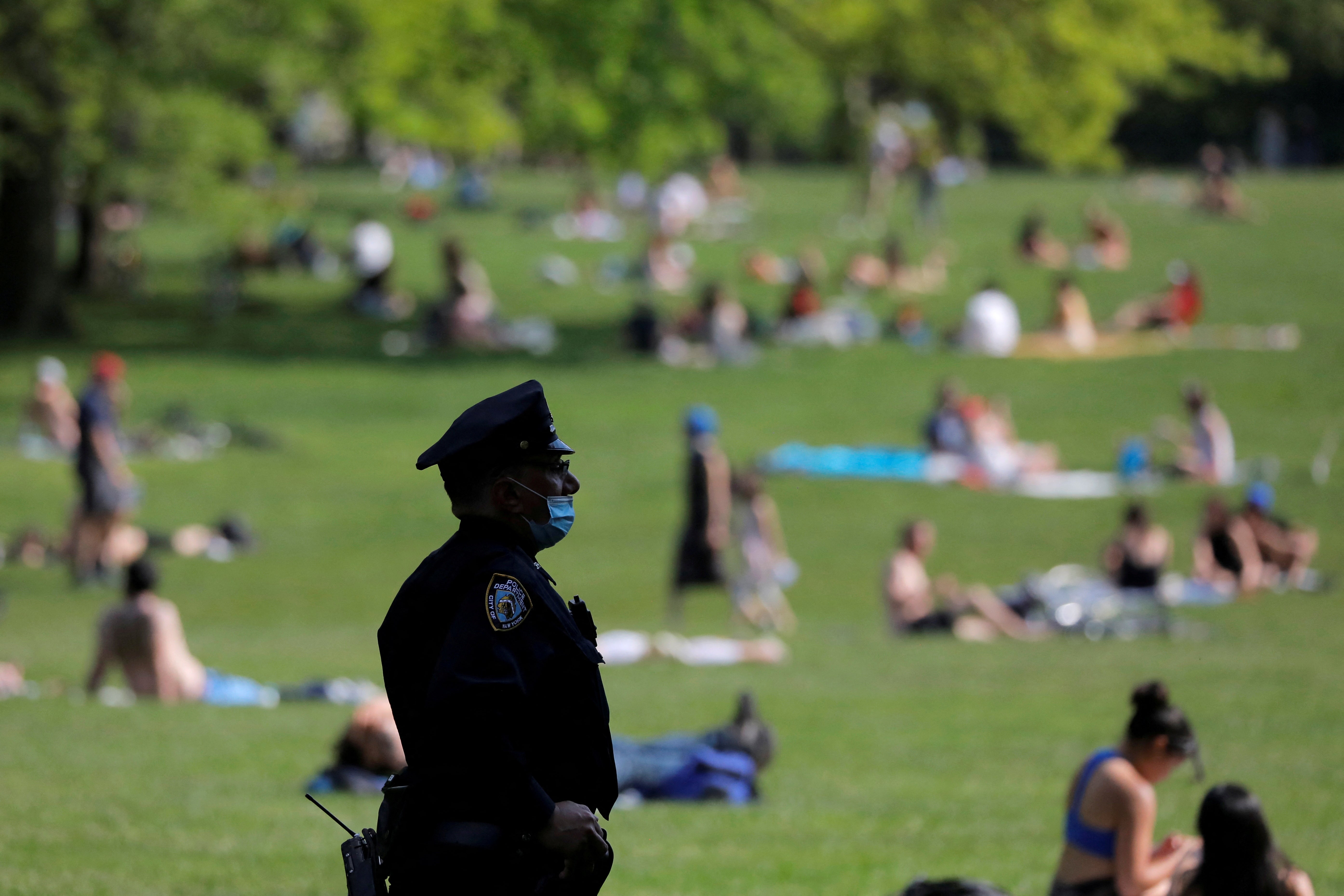 A New York City Police Department officer wearing a protective face mask watches as people gather in the Sheep Meadow in Central Park