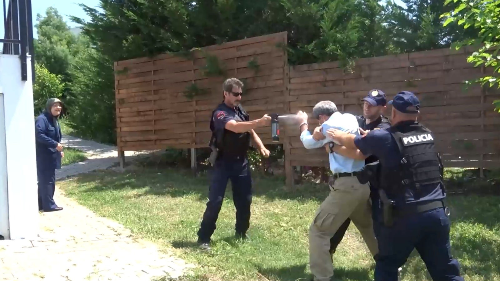 An unidentified man is restrained by two police officers and sprayed with a nonlethal chemical weapon during a police raid on Ashraf III