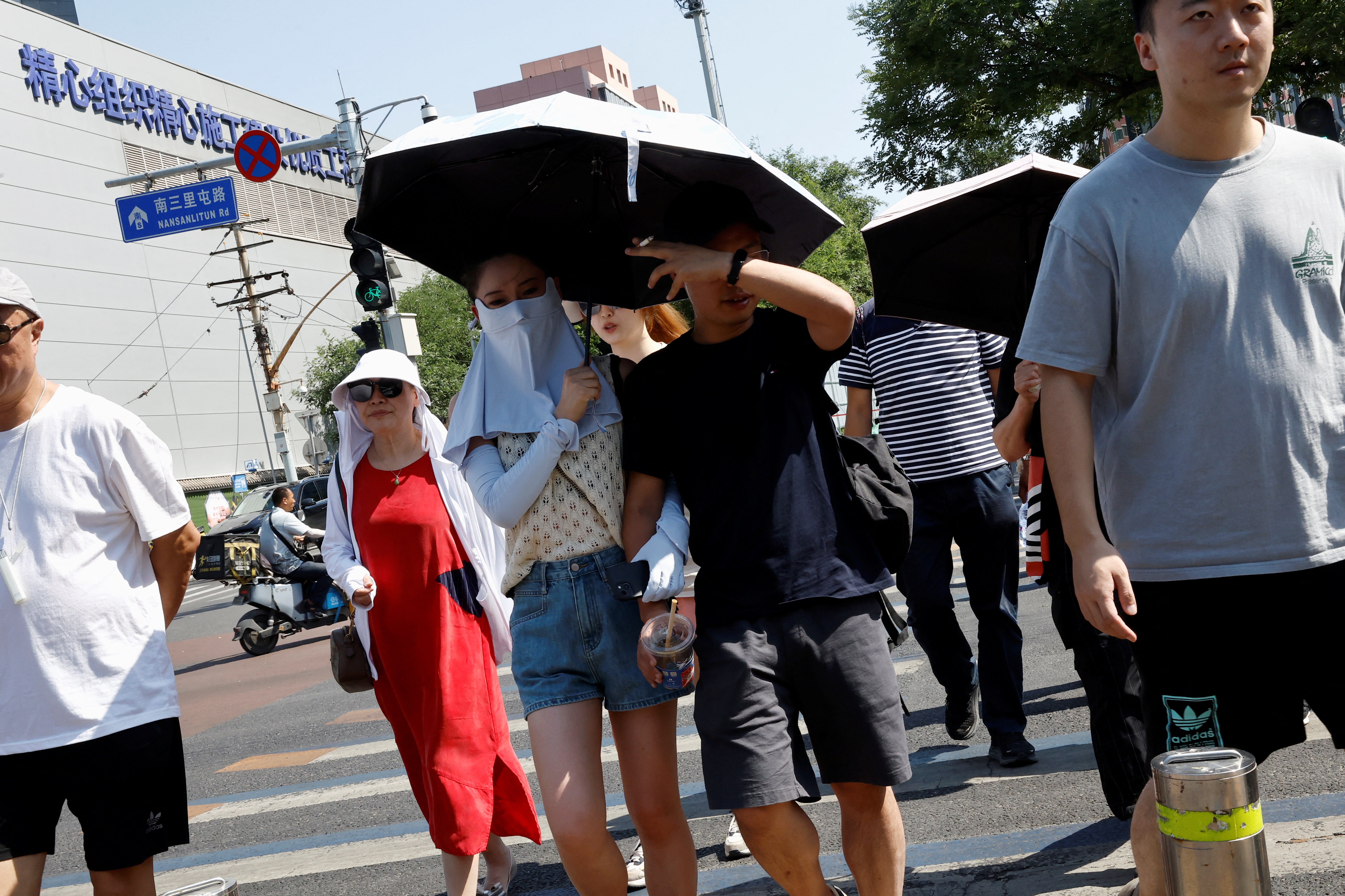 People shield themselves with umbrellas and face masks from the sun amid an orange alert for heatwave in Beijing