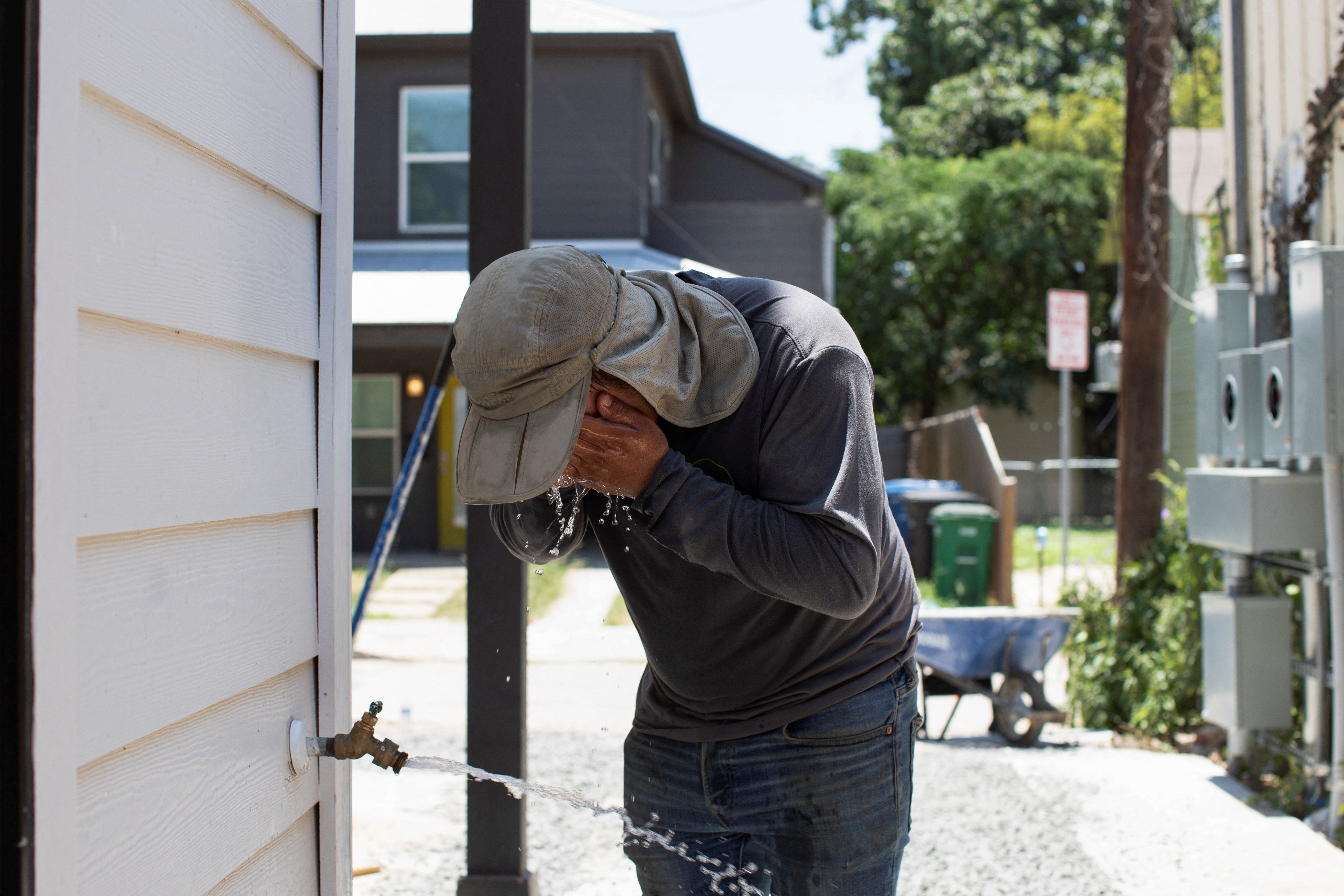 Fernando Oviedo splashes his face with water in between placing gravel at a new build in a residential neighborhood in the middle of the day during a period of hot weather in San Antonio, Texas